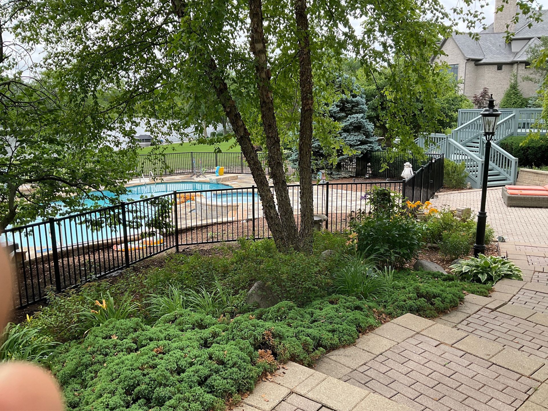 Pool area with landscaping, trees, and a wrought-iron fence.