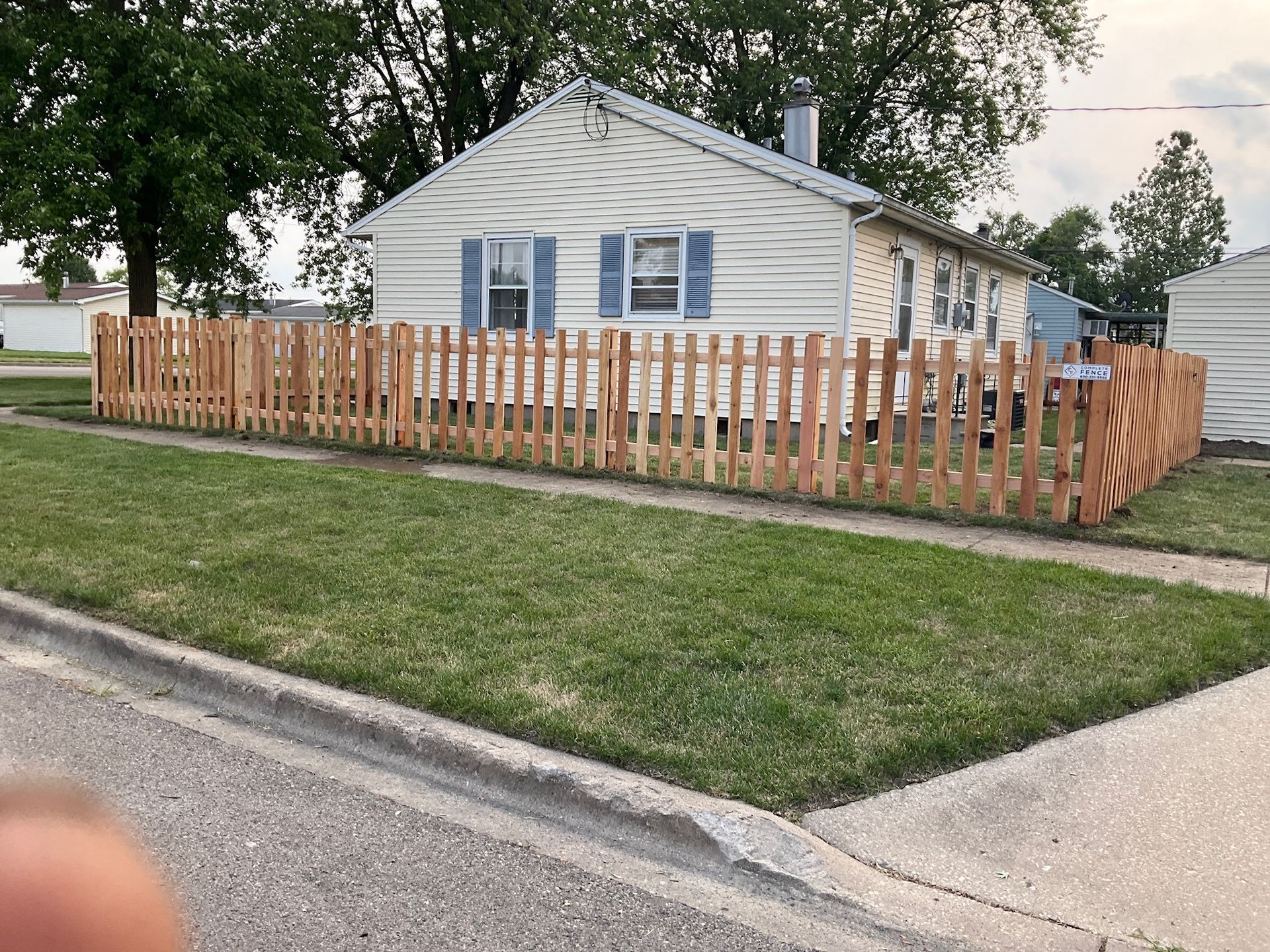 A light-colored house with blue shutters and a new wooden picket fence around the yard on a sunny day.