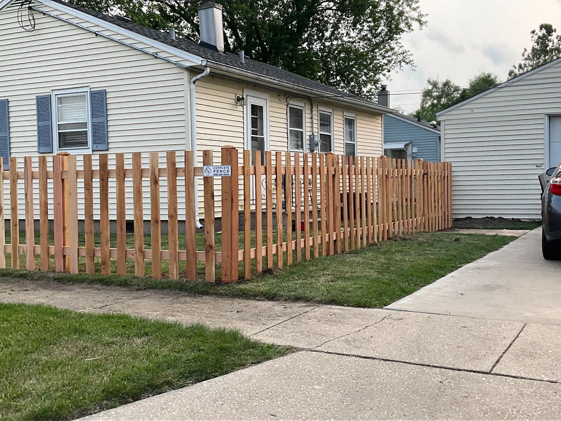 Wooden picket fence in front of a house.  Green grass and a sidewalk lead up to the home.
