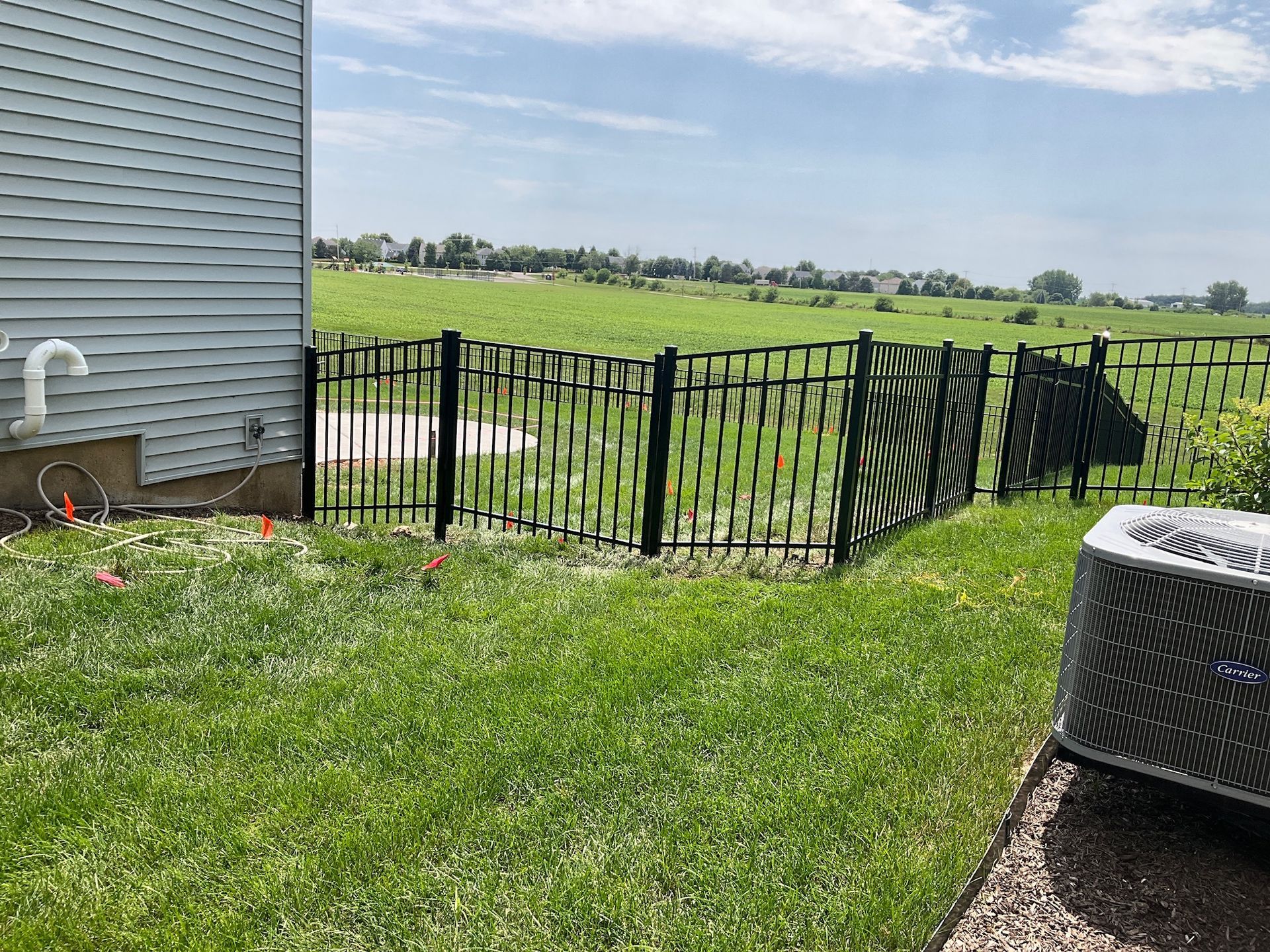 Black metal fence in a green yard, next to a house with an air conditioner unit.