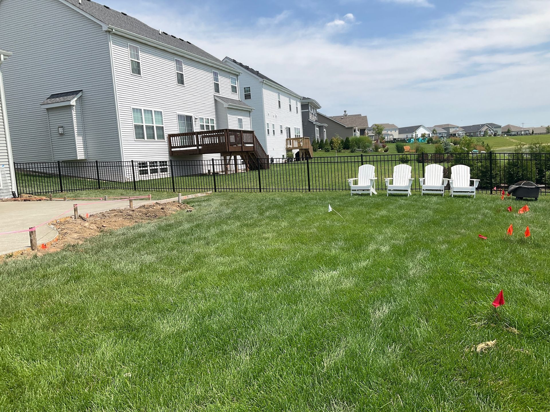 Backyard with green grass, white chairs, black fence, and two-story house.