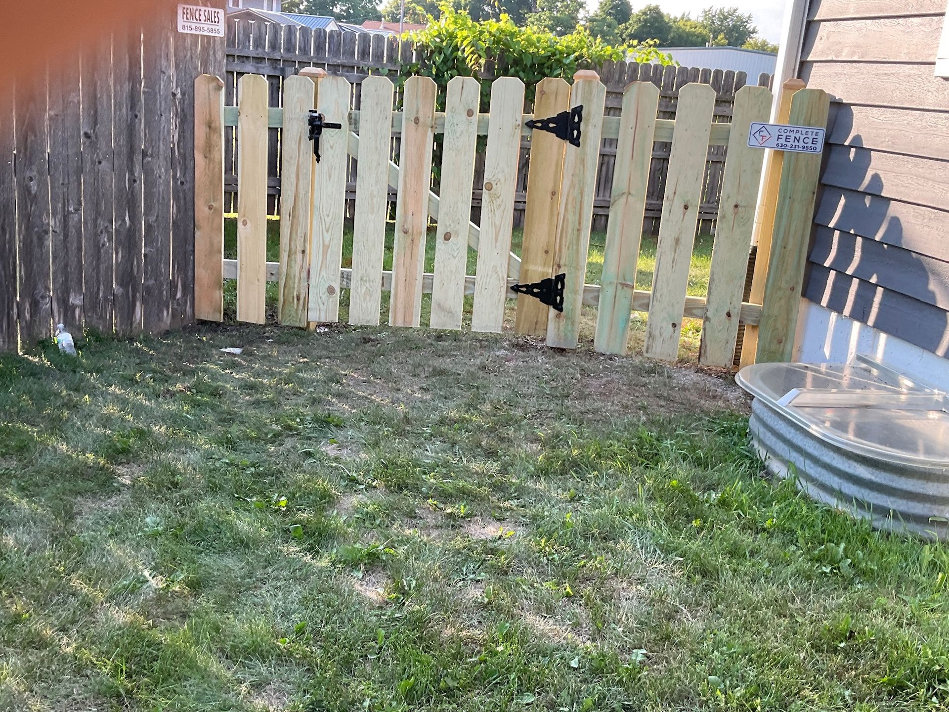 Wooden picket fence with gate, grassy yard, metal tub.