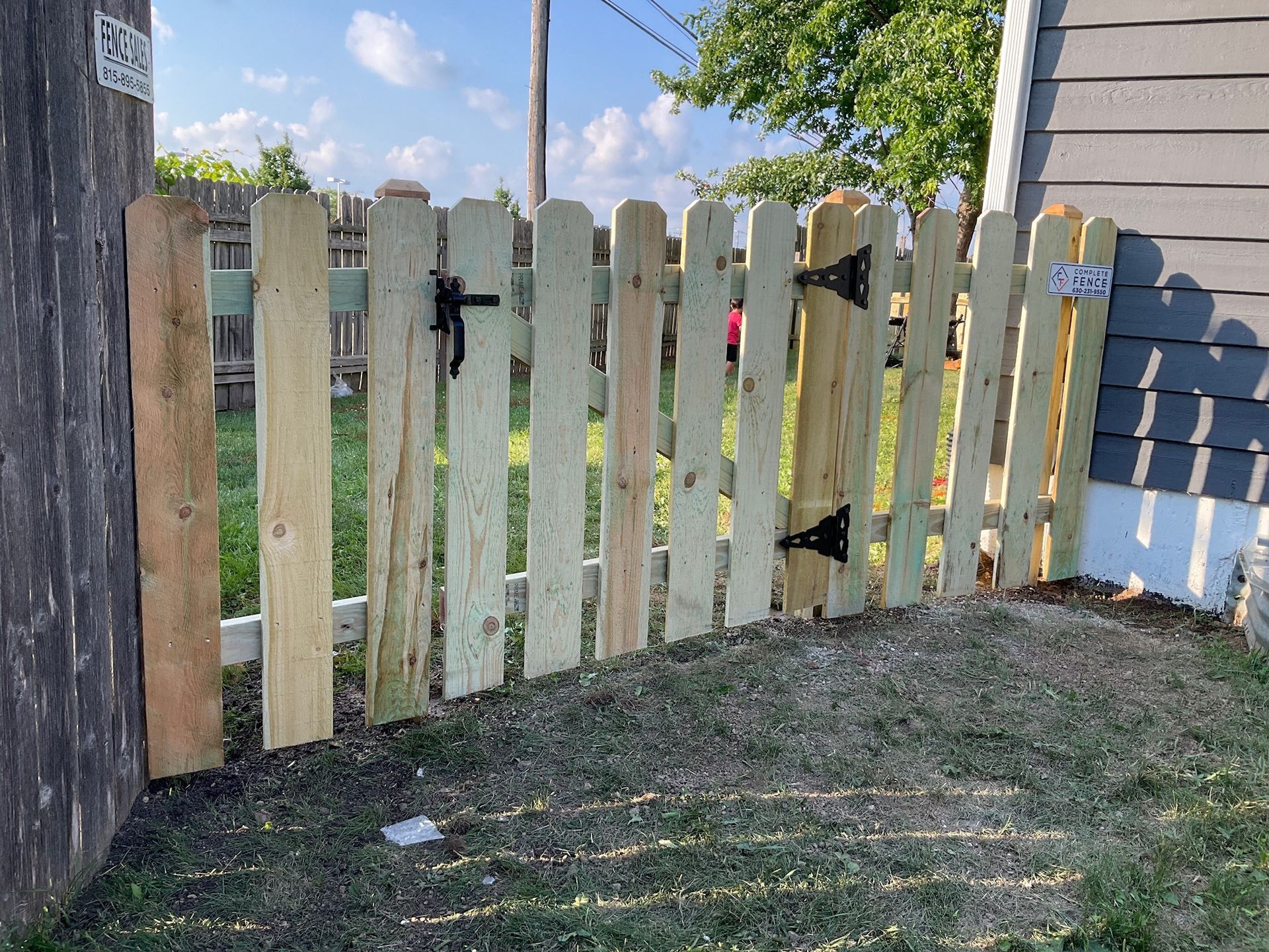 Wooden picket fence with two gates, attached to a gray building.