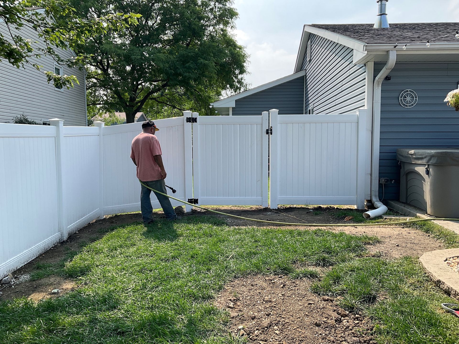 Person spraying near a white vinyl fence in a backyard.