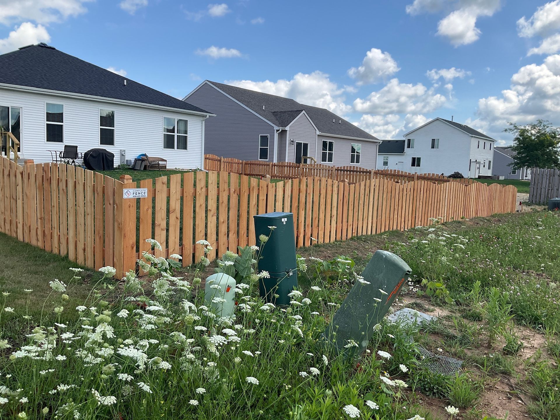 Wooden fence between houses with wildflowers in the foreground and a blue sky overhead.