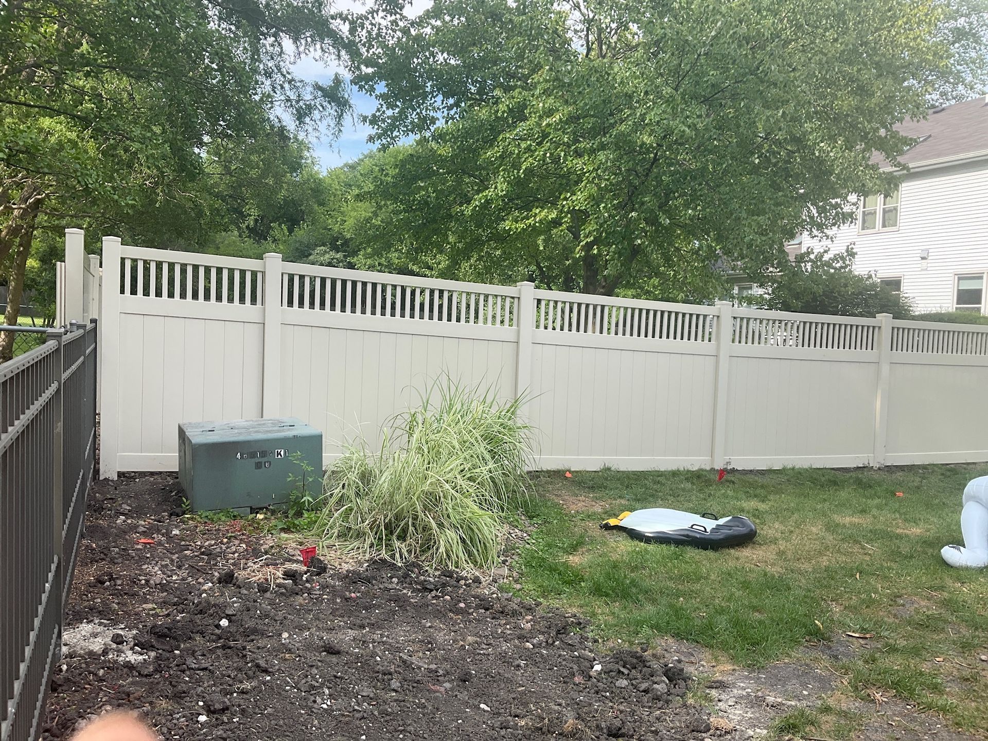 Beige vinyl fence in a backyard, with trees and a house in the background.