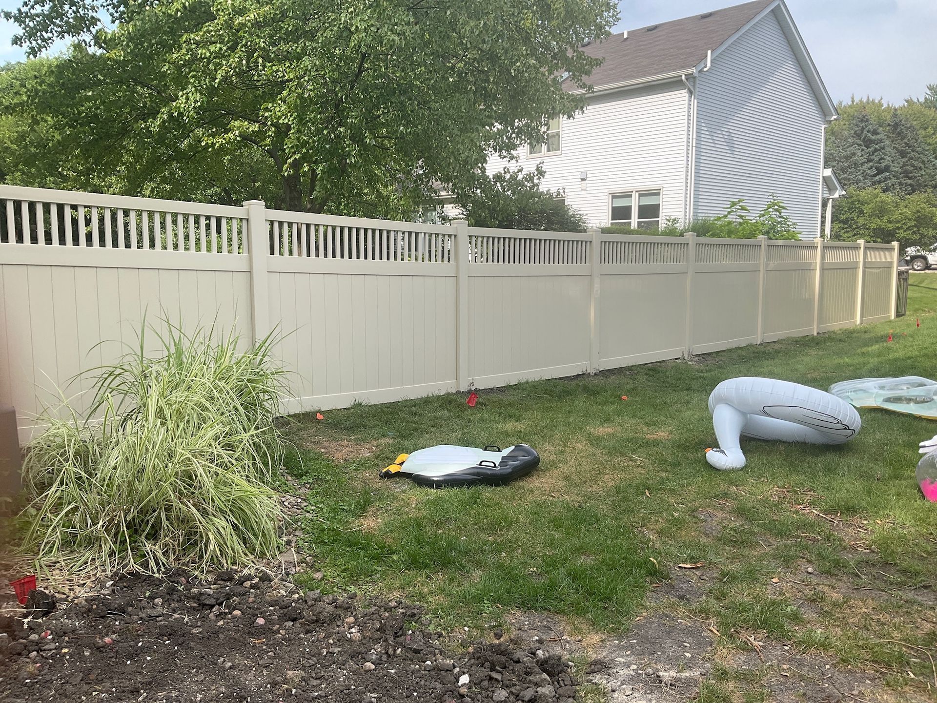 Tan vinyl fence in a backyard with grass, a house, and inflatable toys.