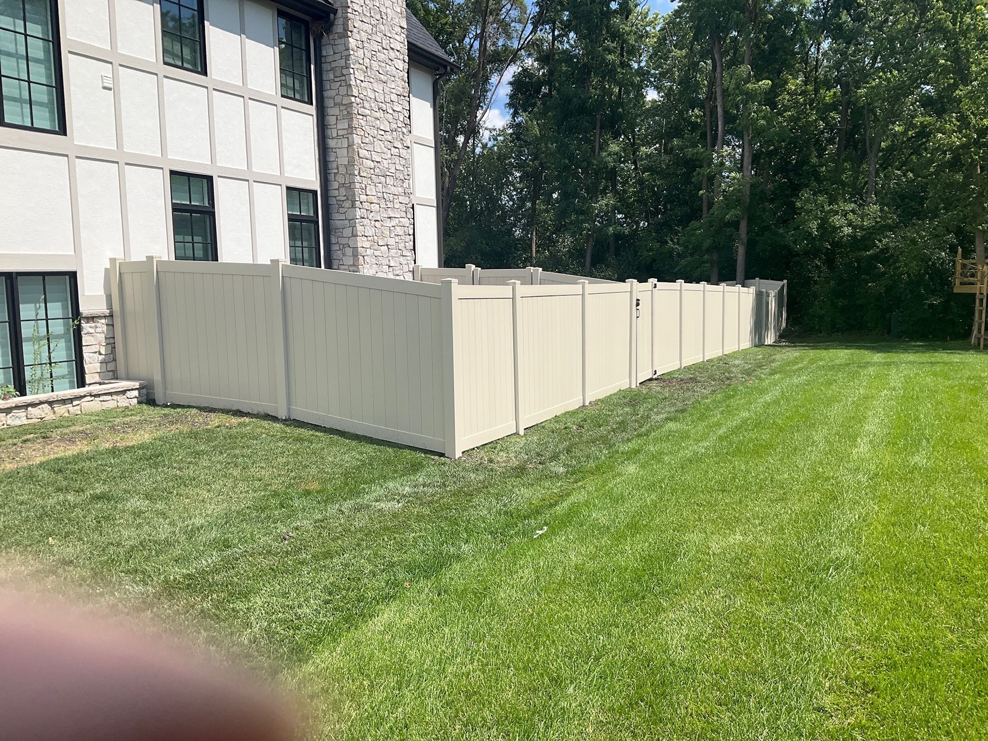 Beige vinyl fence encloses a green lawn, next to a two-story building with a chimney.
