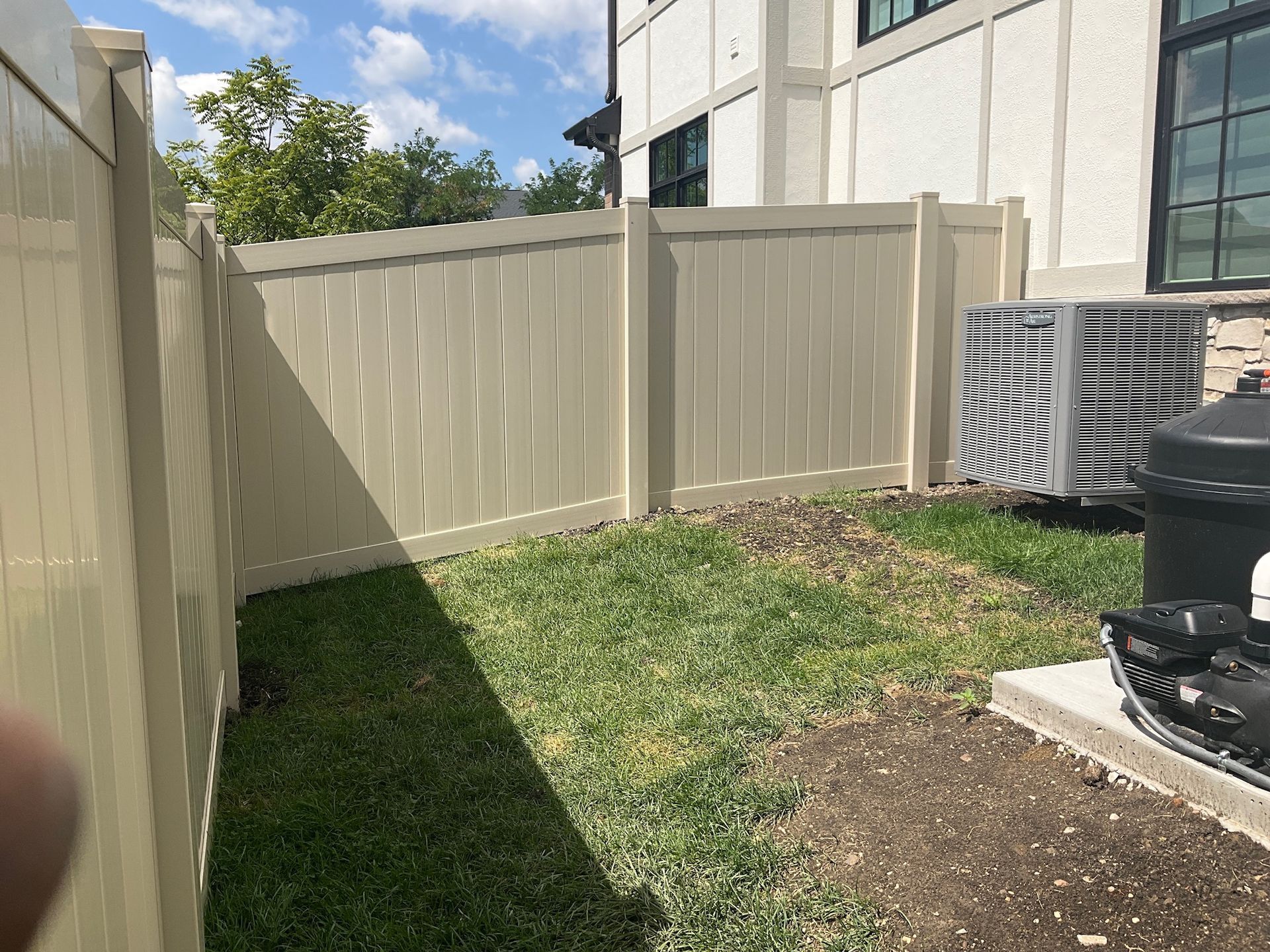 Tan vinyl fence encloses a small, grassy backyard with an air conditioner unit.