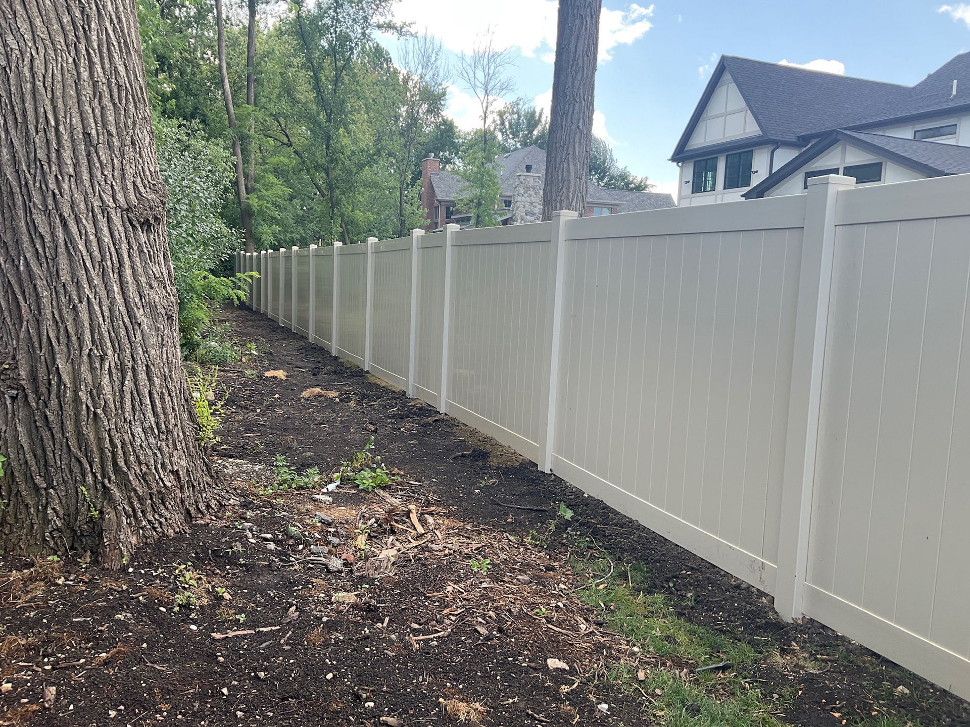 Beige vinyl fence along a wooded area, with a house in the background.