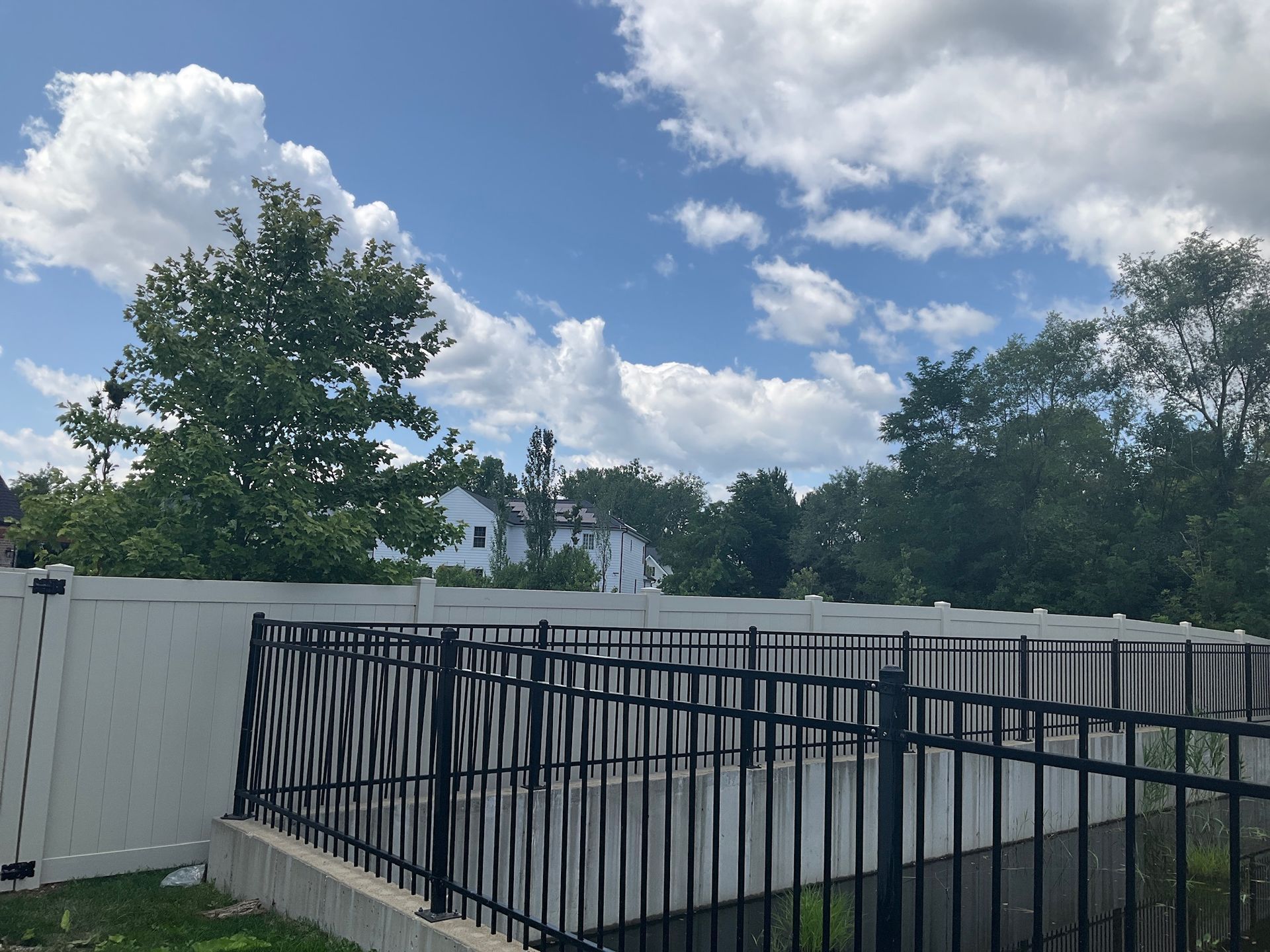 Fence in front of a building and trees under a cloudy sky.