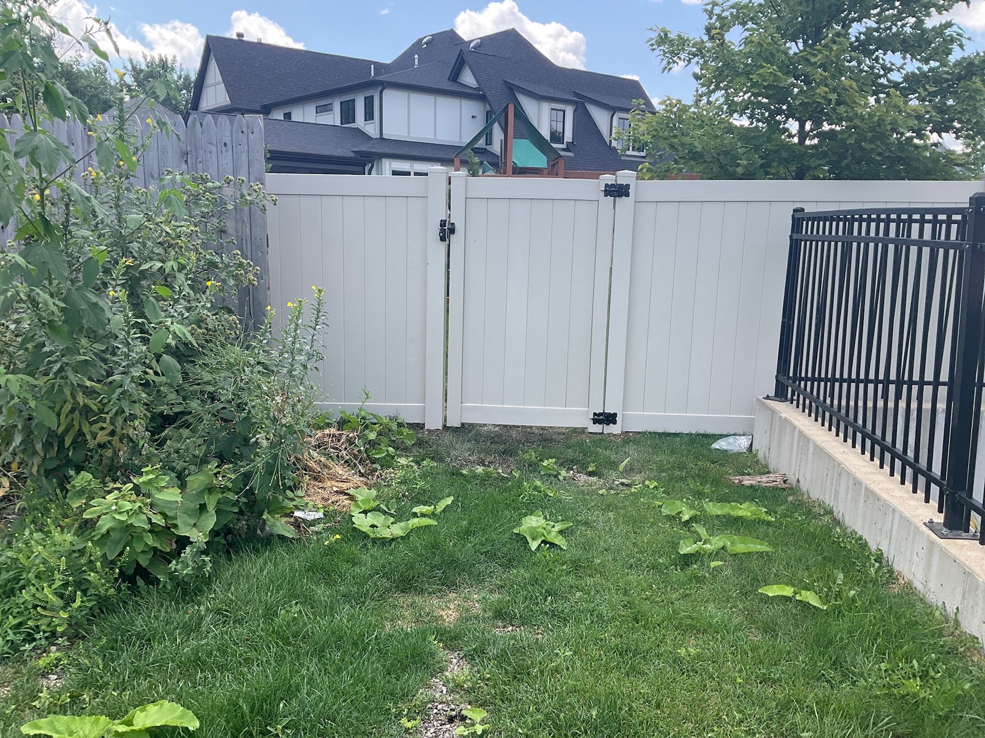 White vinyl fence with gate, grassy yard, and partially visible house in the background.