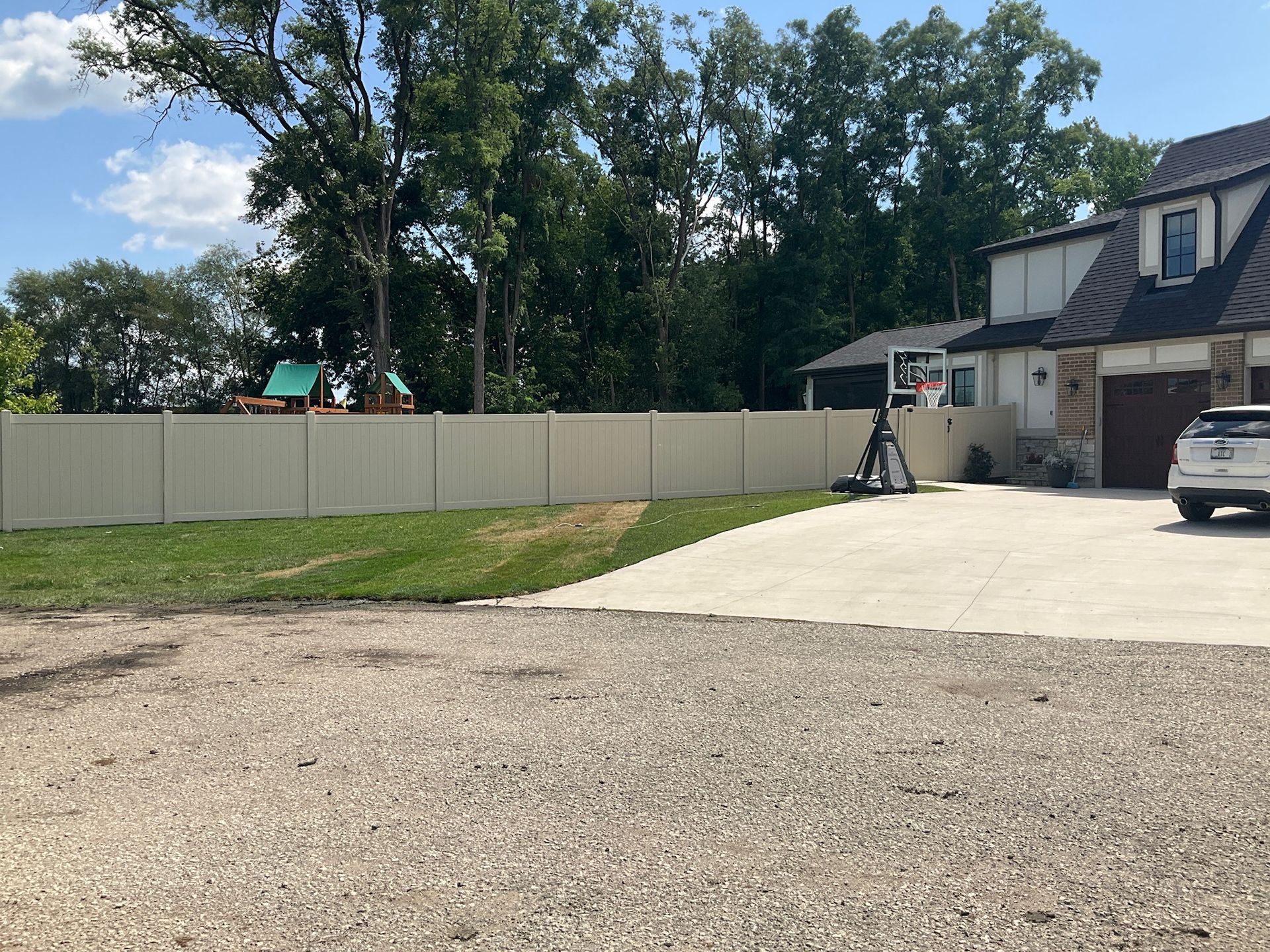 Beige fence in front yard with a basketball hoop and a two-story house.