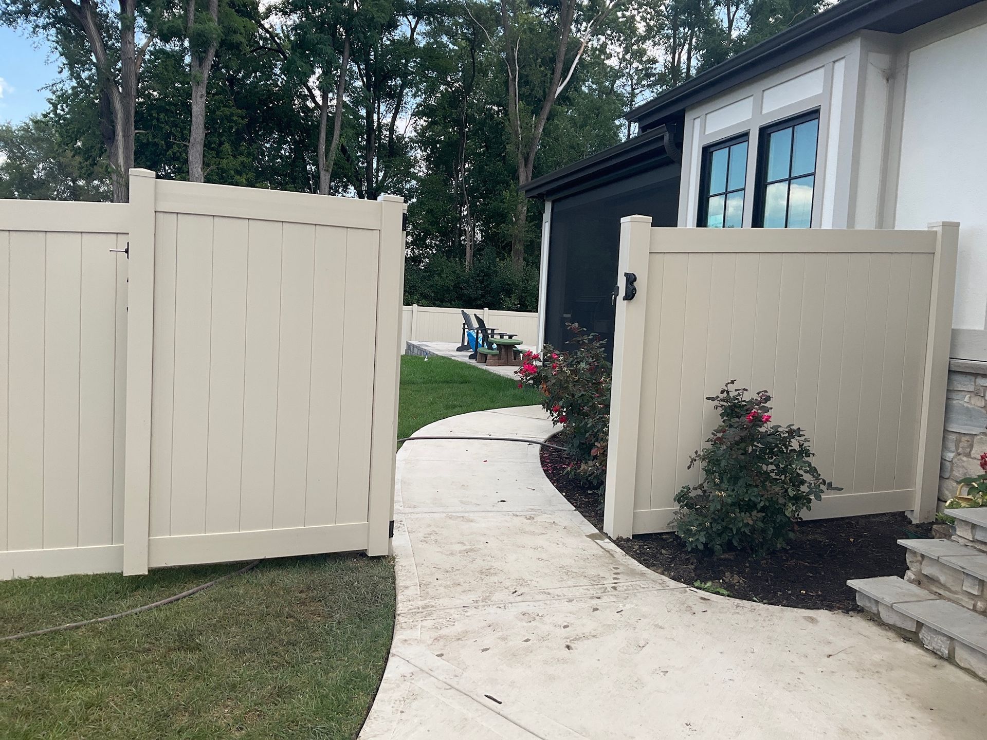 Beige vinyl fence with a gate, concrete path, and house with black trim.