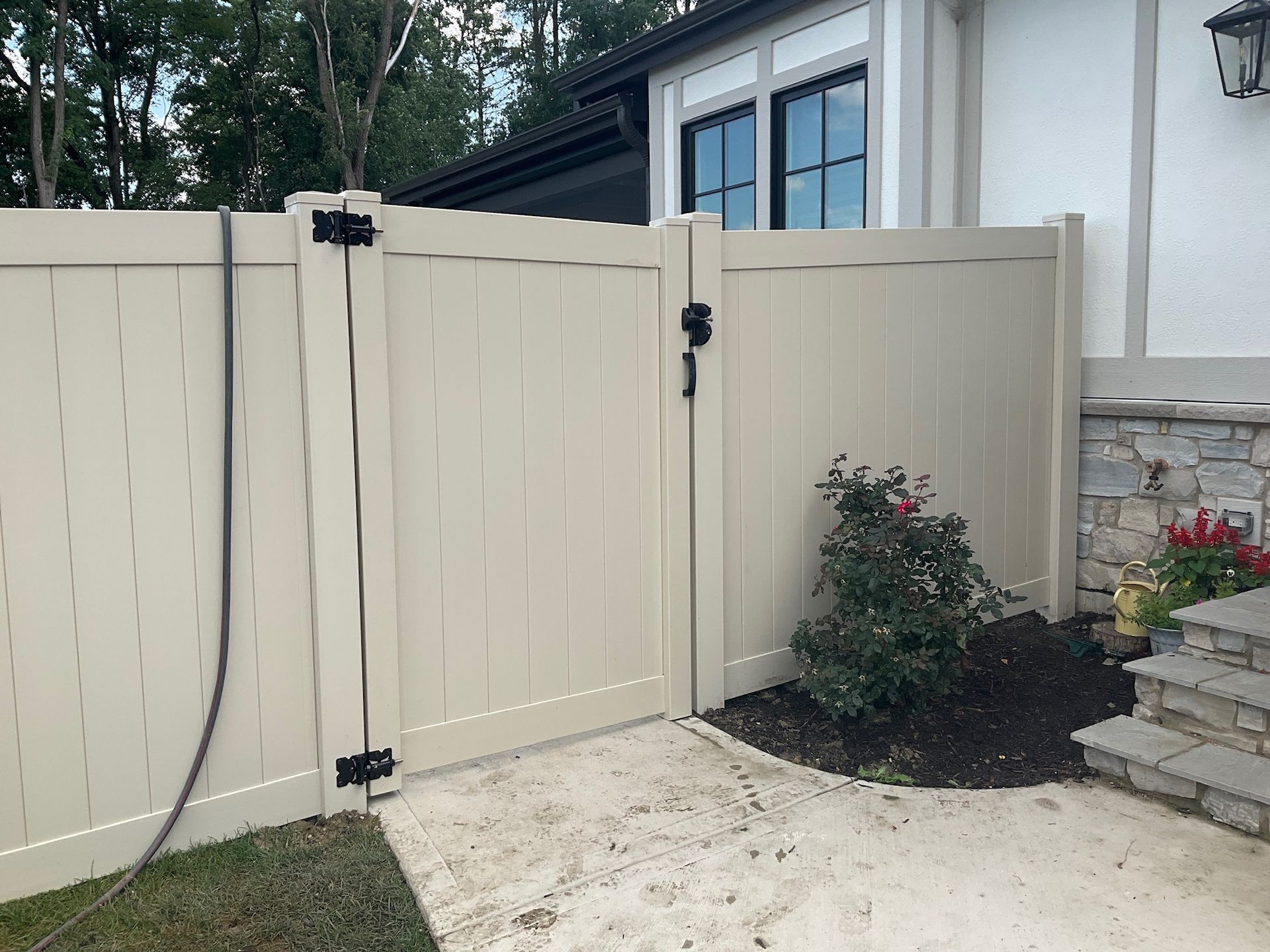 Tan vinyl gate with black hinges and handle, next to a building with stone accents.