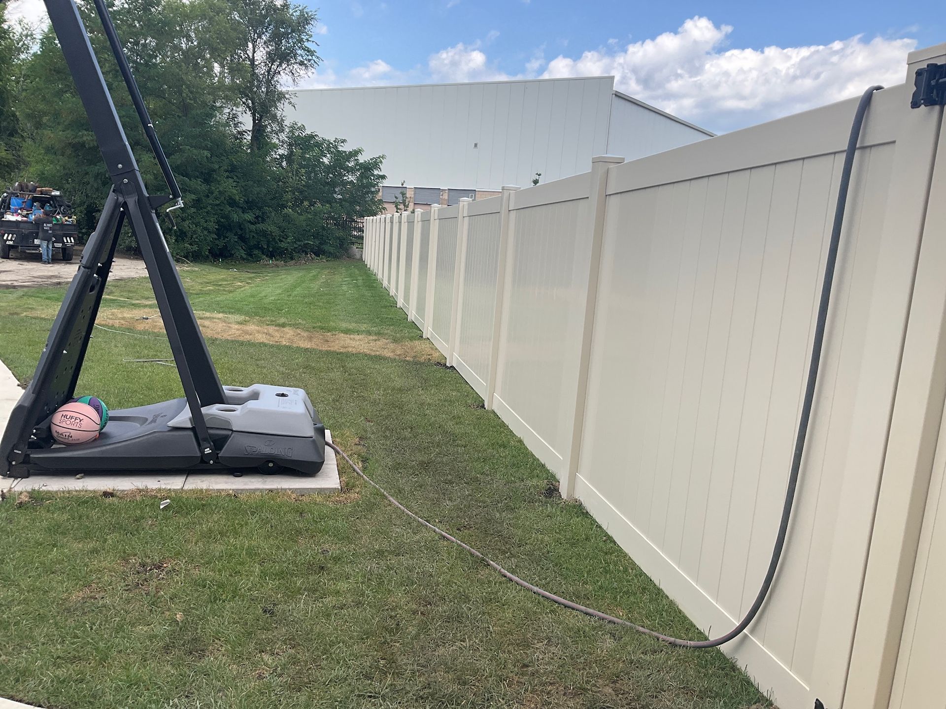 A person lies on a swing structure near a long beige fence outdoors on a sunny day.