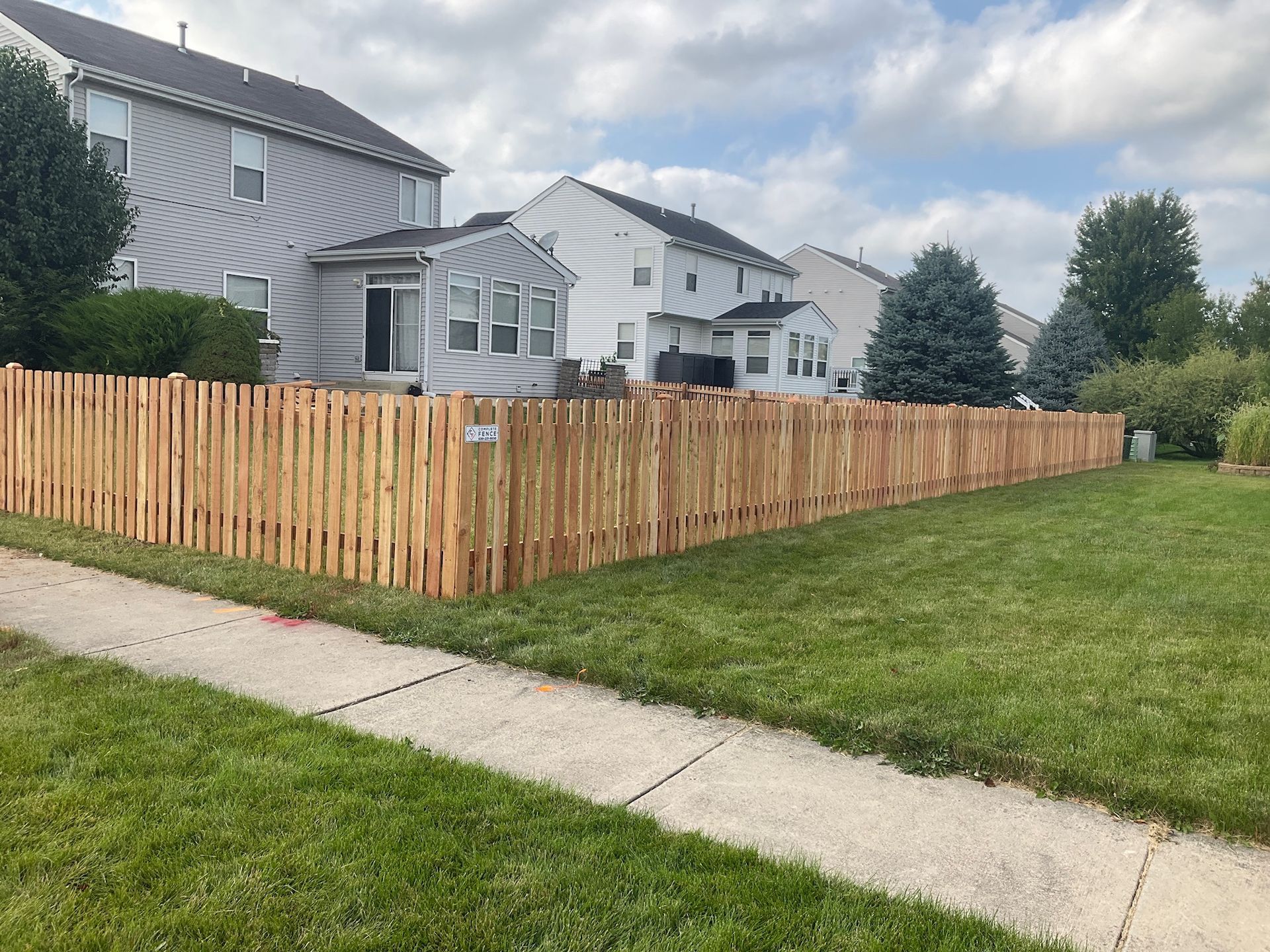 Wooden fence surrounding a grassy backyard with two-story houses under a cloudy sky.