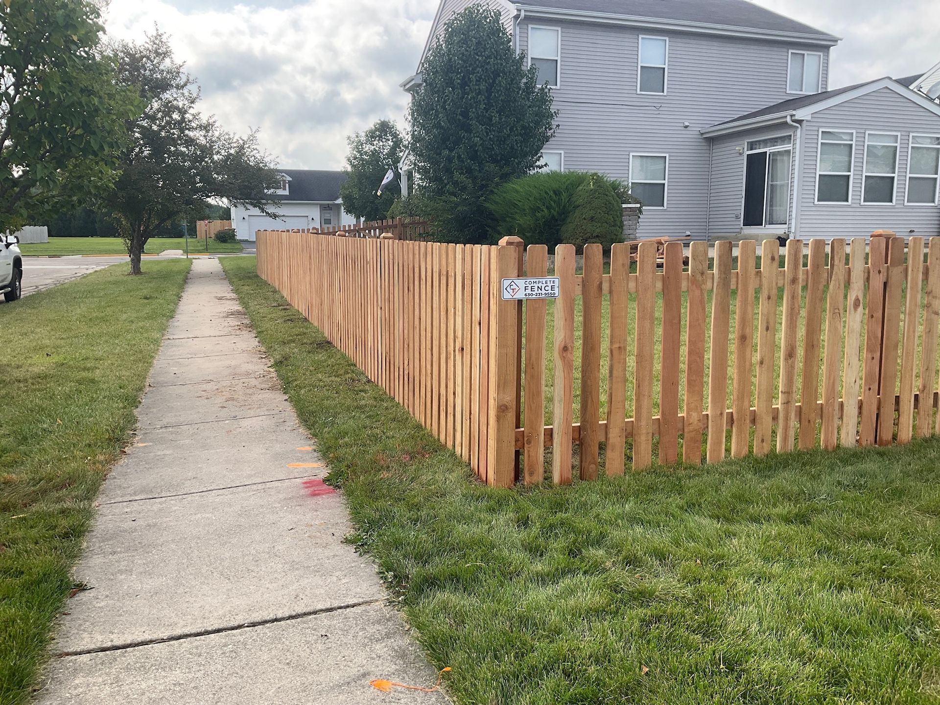 A wooden fence along a sidewalk in front of a house.