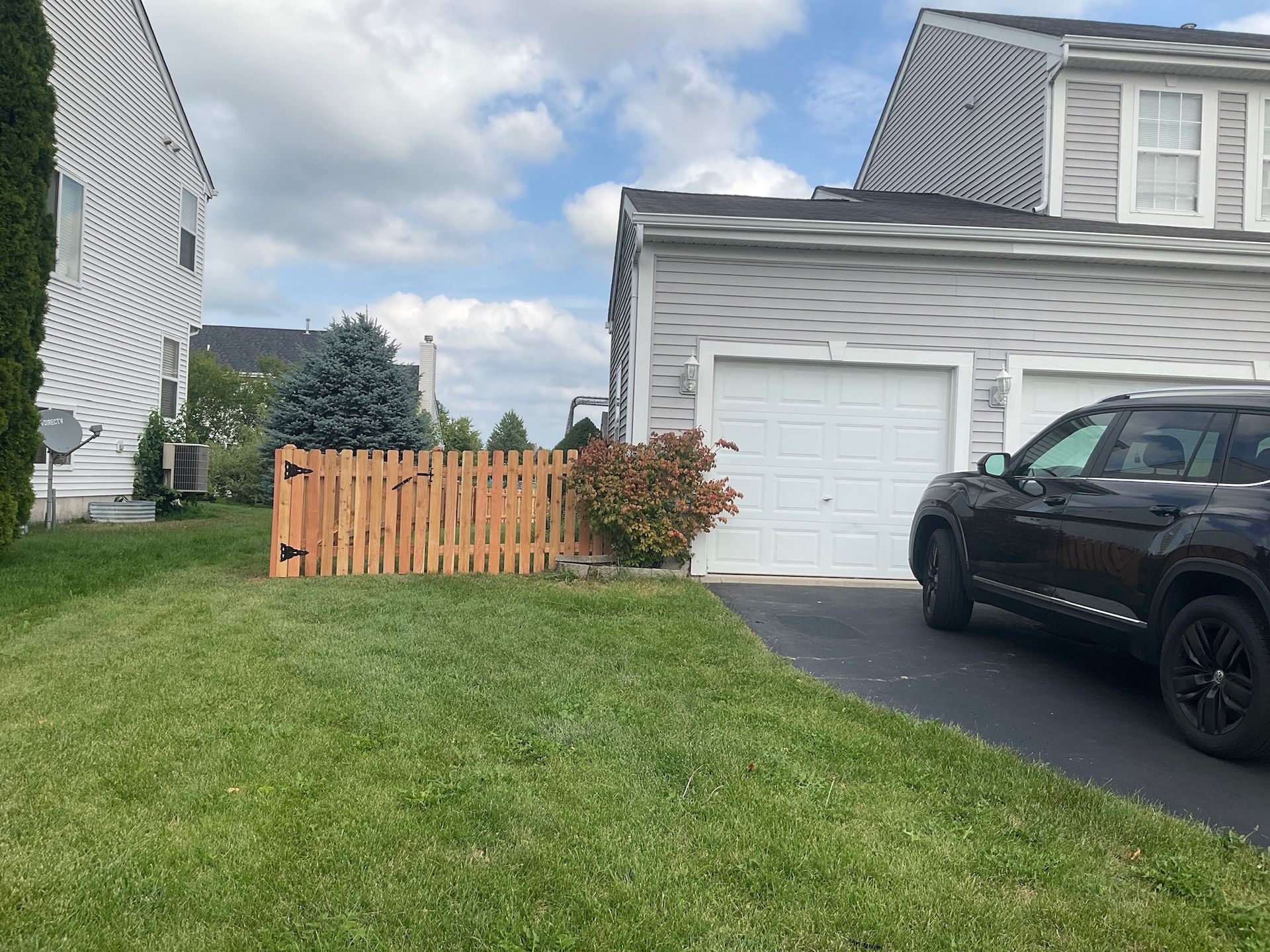 Lawn, wooden fence, garage, car parked on driveway under a cloudy sky.