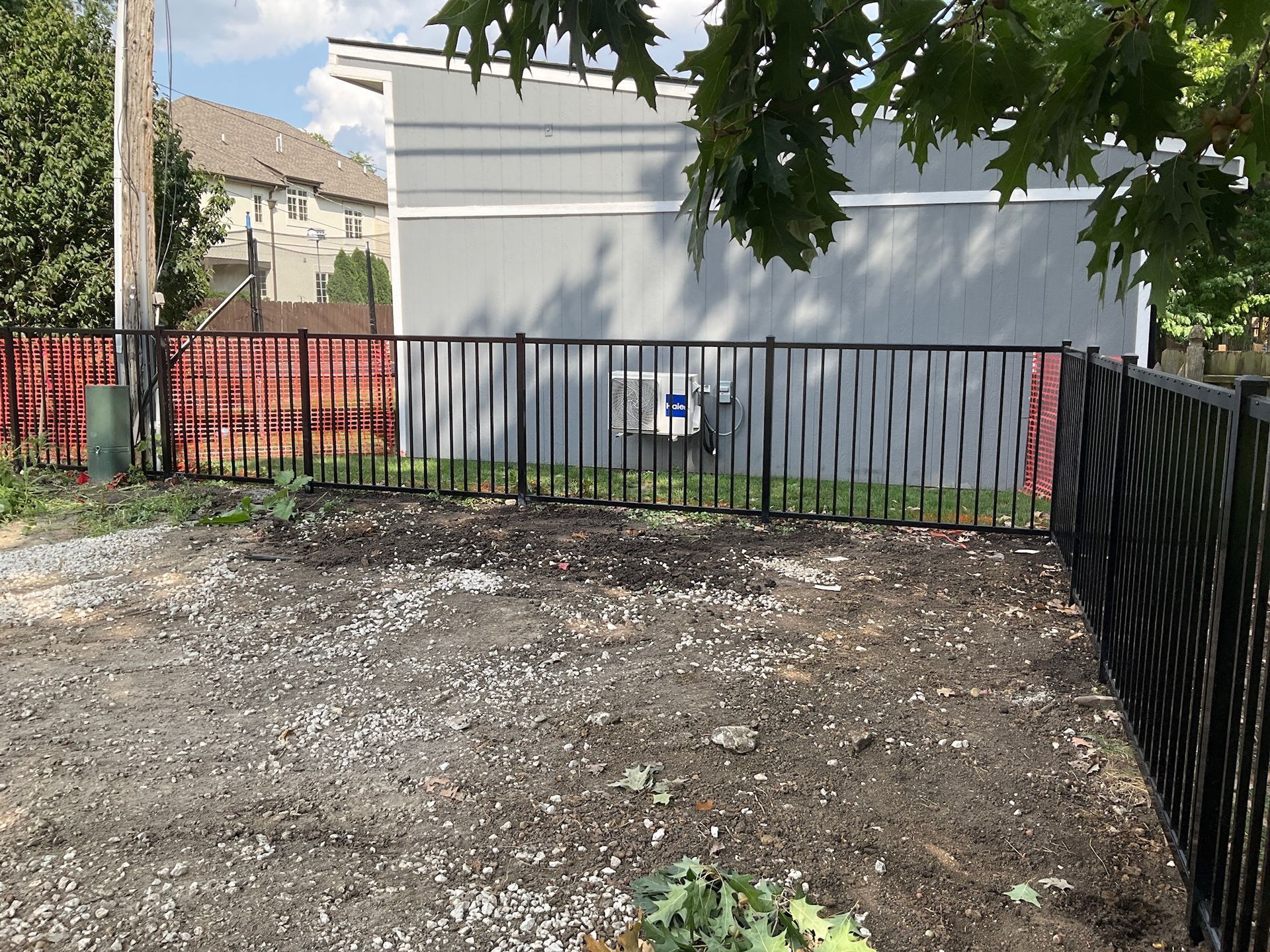 Black metal fence enclosing a gravel yard with a light gray building in the background.