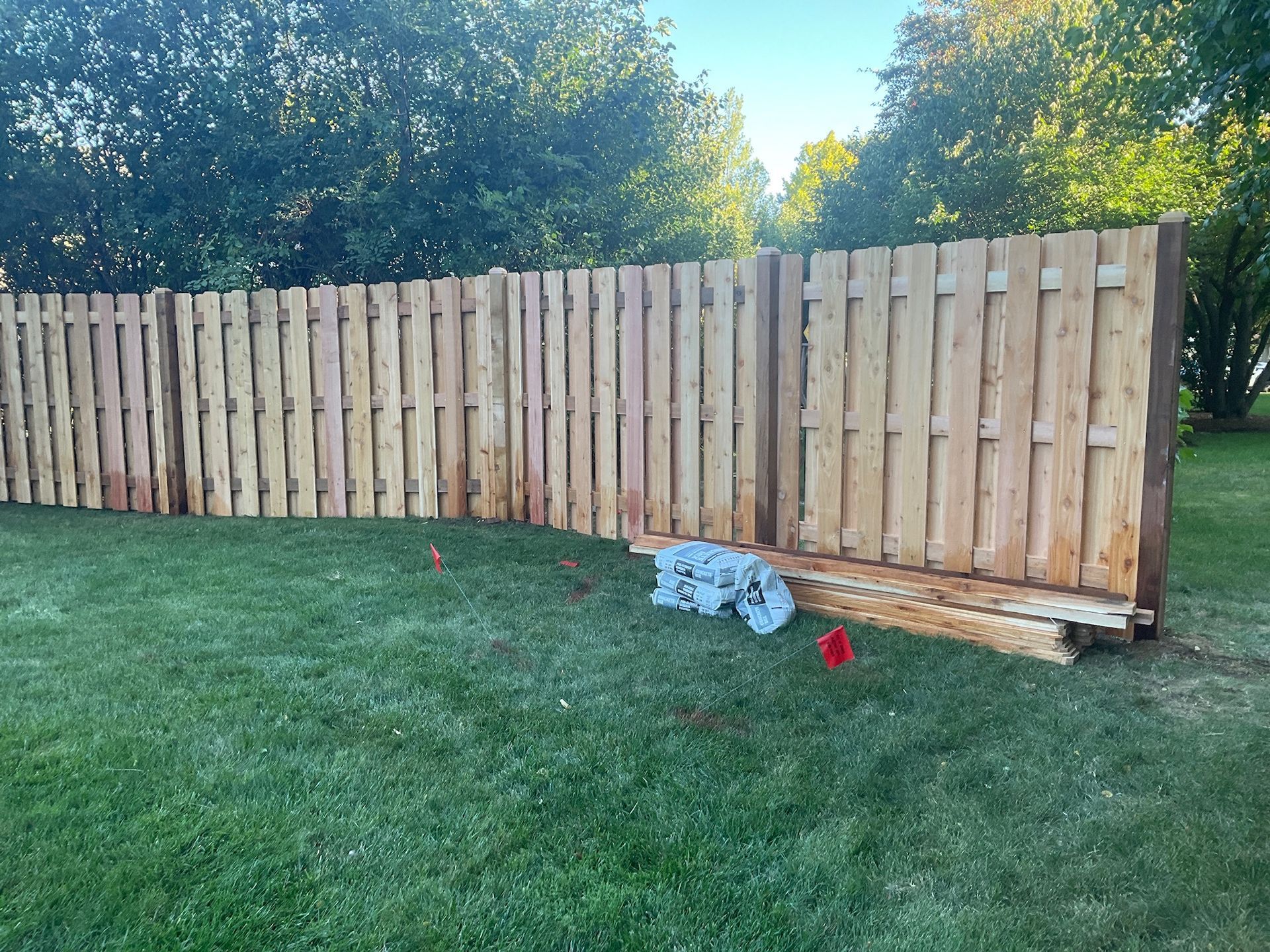 A weathered wooden fence in a grassy yard under a blue sky, with some damage at the base.