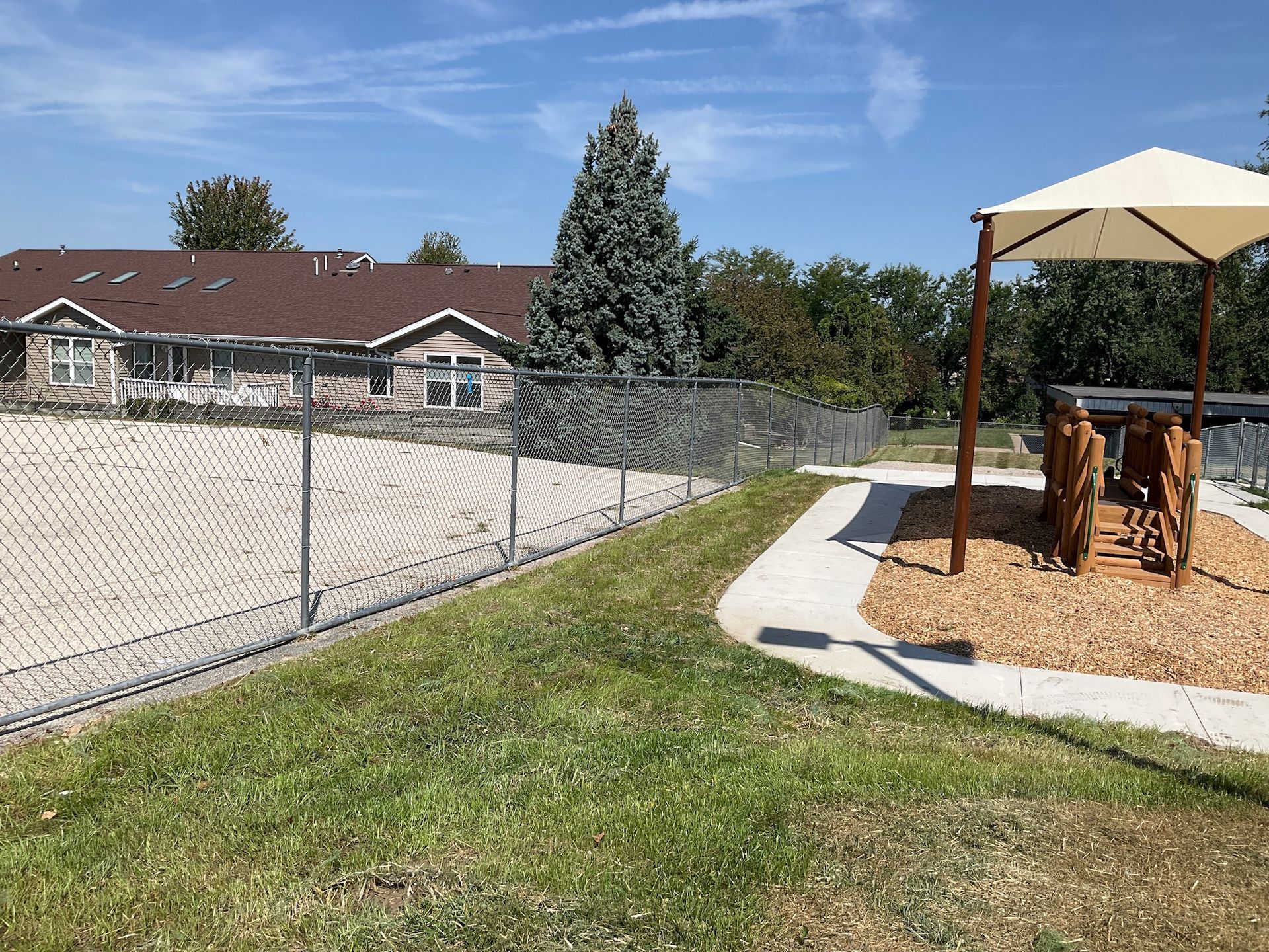 Grassy area with chain link fence, playground structure, and building with a brown roof.