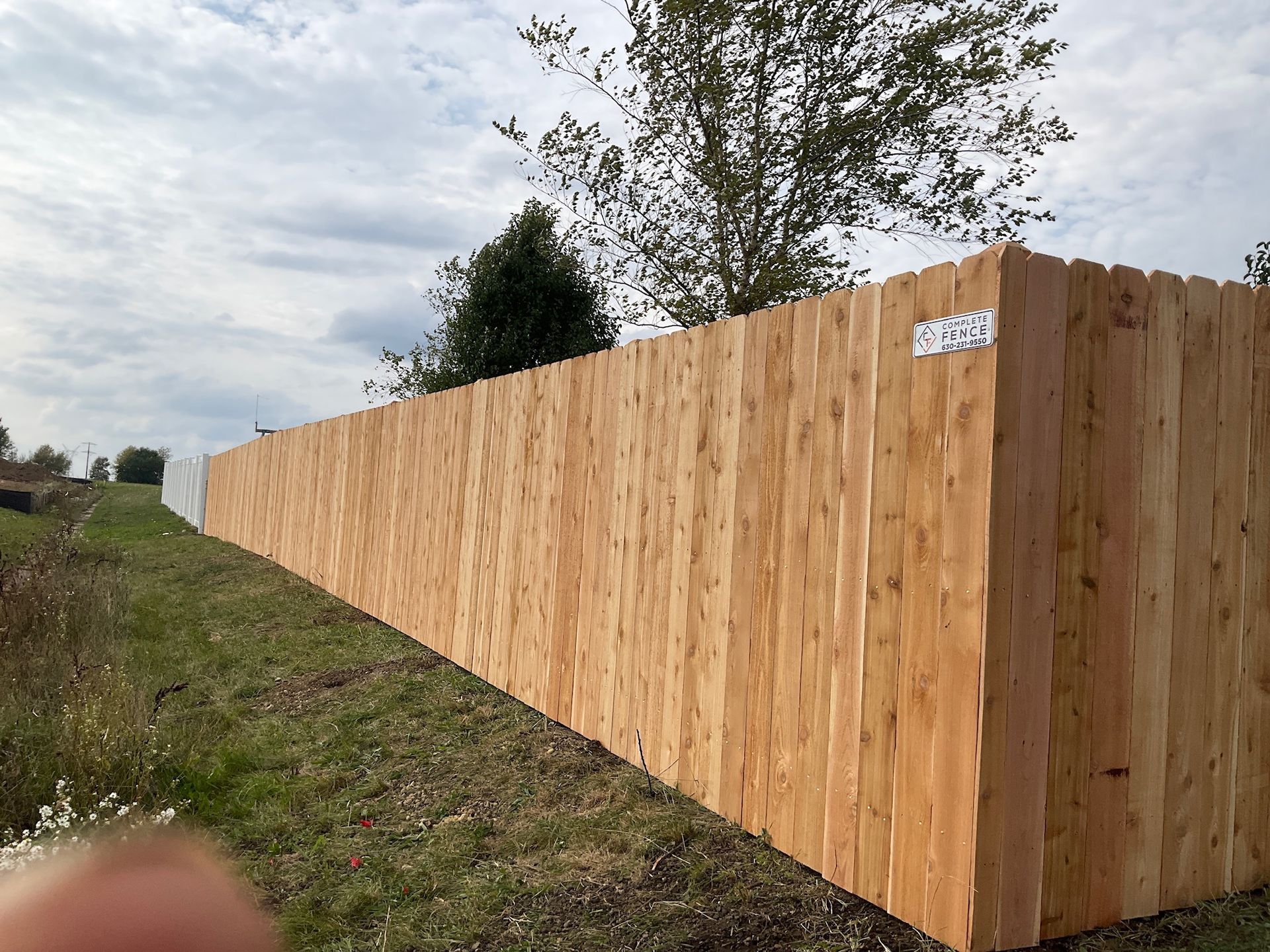 Wooden fence along a grassy slope, with a cloudy sky in the background.