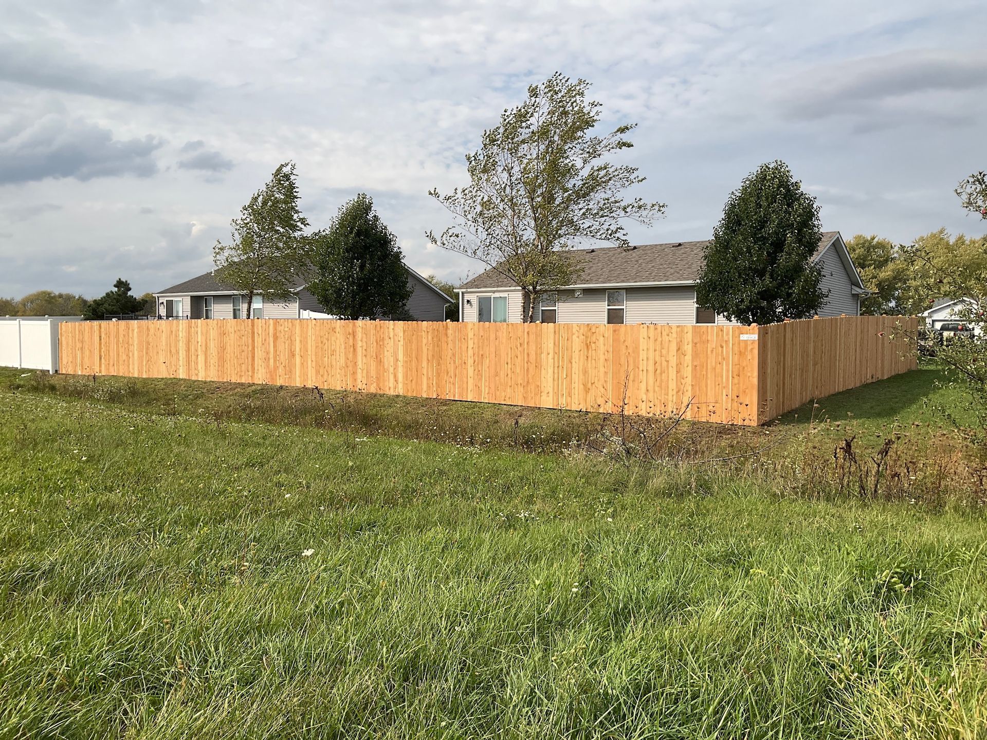 Wooden fence surrounding two houses in a grassy field under an overcast sky.