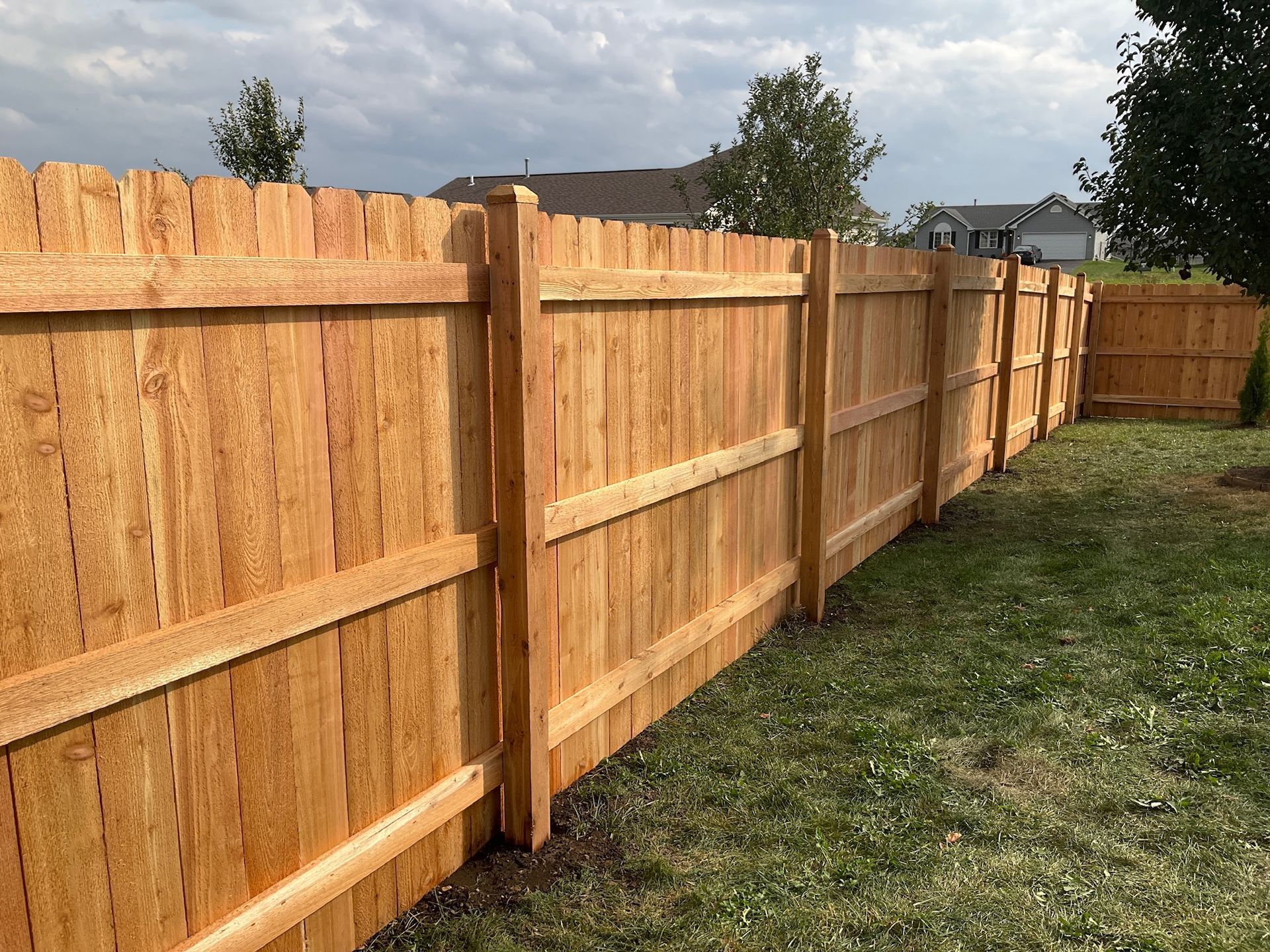 Wooden privacy fence in a grassy yard under a cloudy sky.