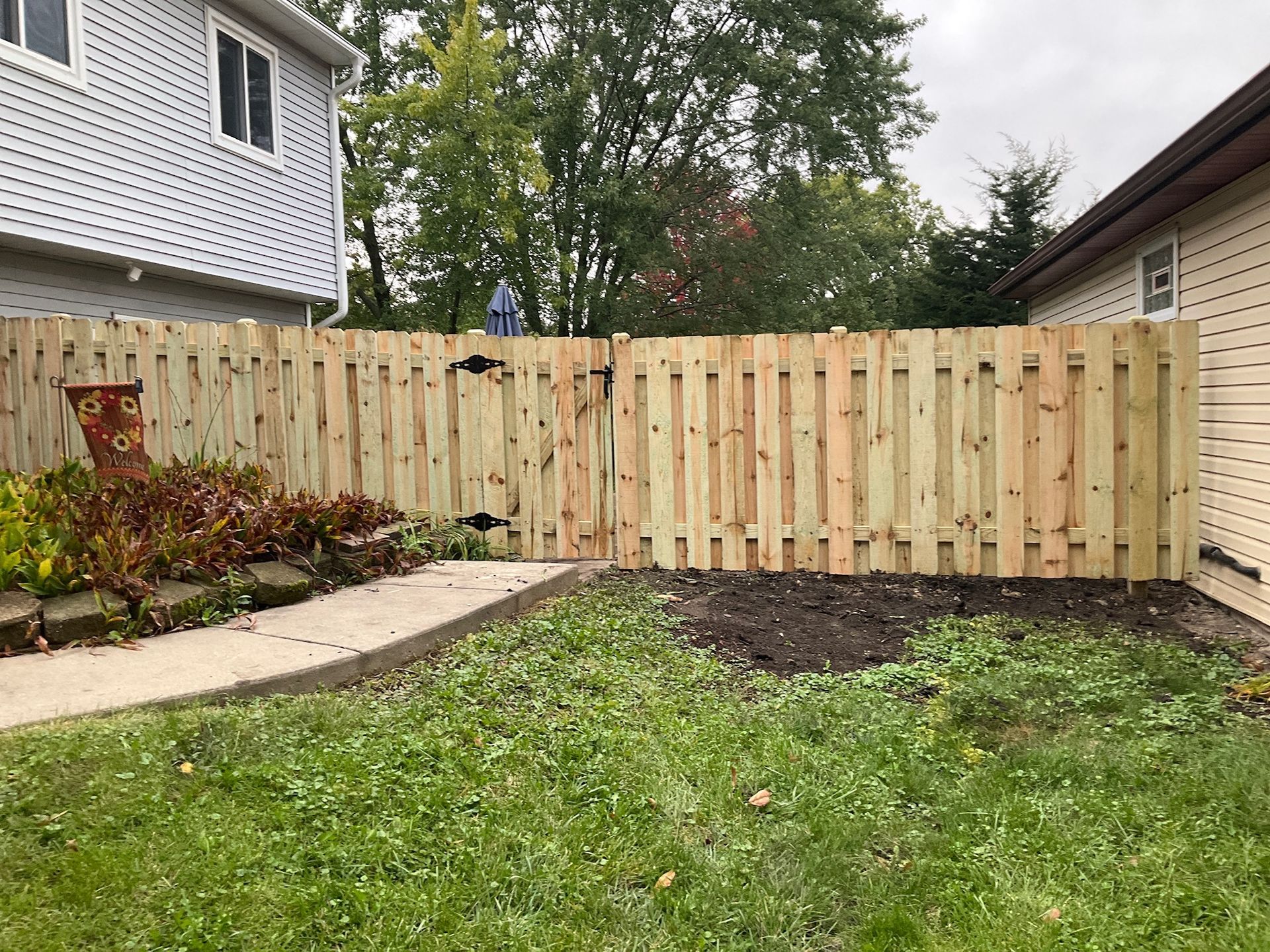 Wooden fence in a backyard between two houses, with a patch of grass and a concrete walkway.