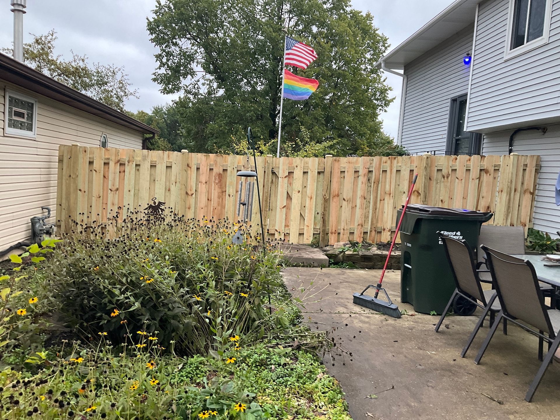 Backyard with wooden fence, garden, trash can, and pride flags.