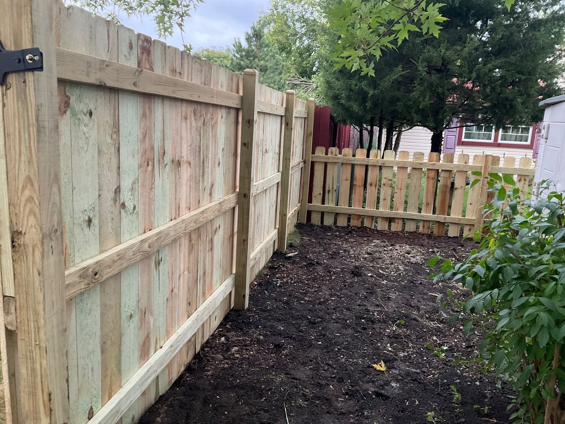 Wooden fence in a yard with a small, picket fence section. Earth is visible in front of the fences.