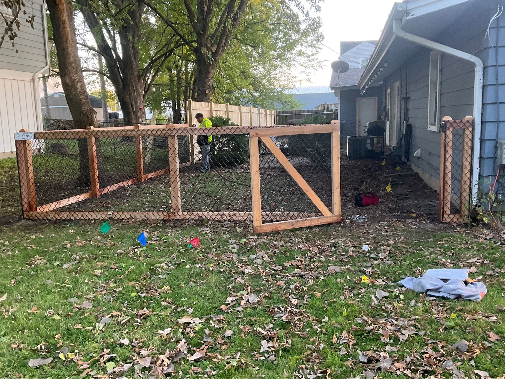 Backyard with a partially built wooden fence and gate. A person works in the background.