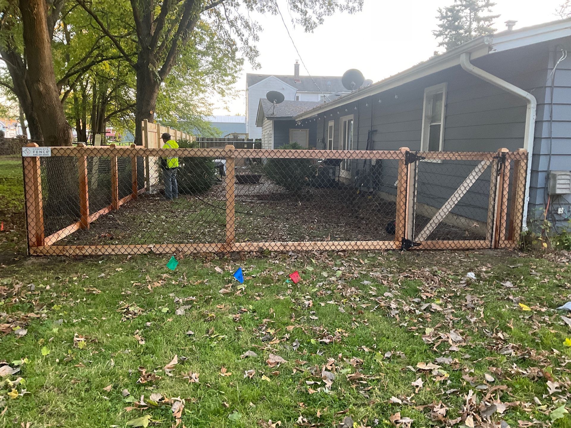 Wooden fence with wire mesh in a backyard, near a house. Man in yellow vest works nearby.