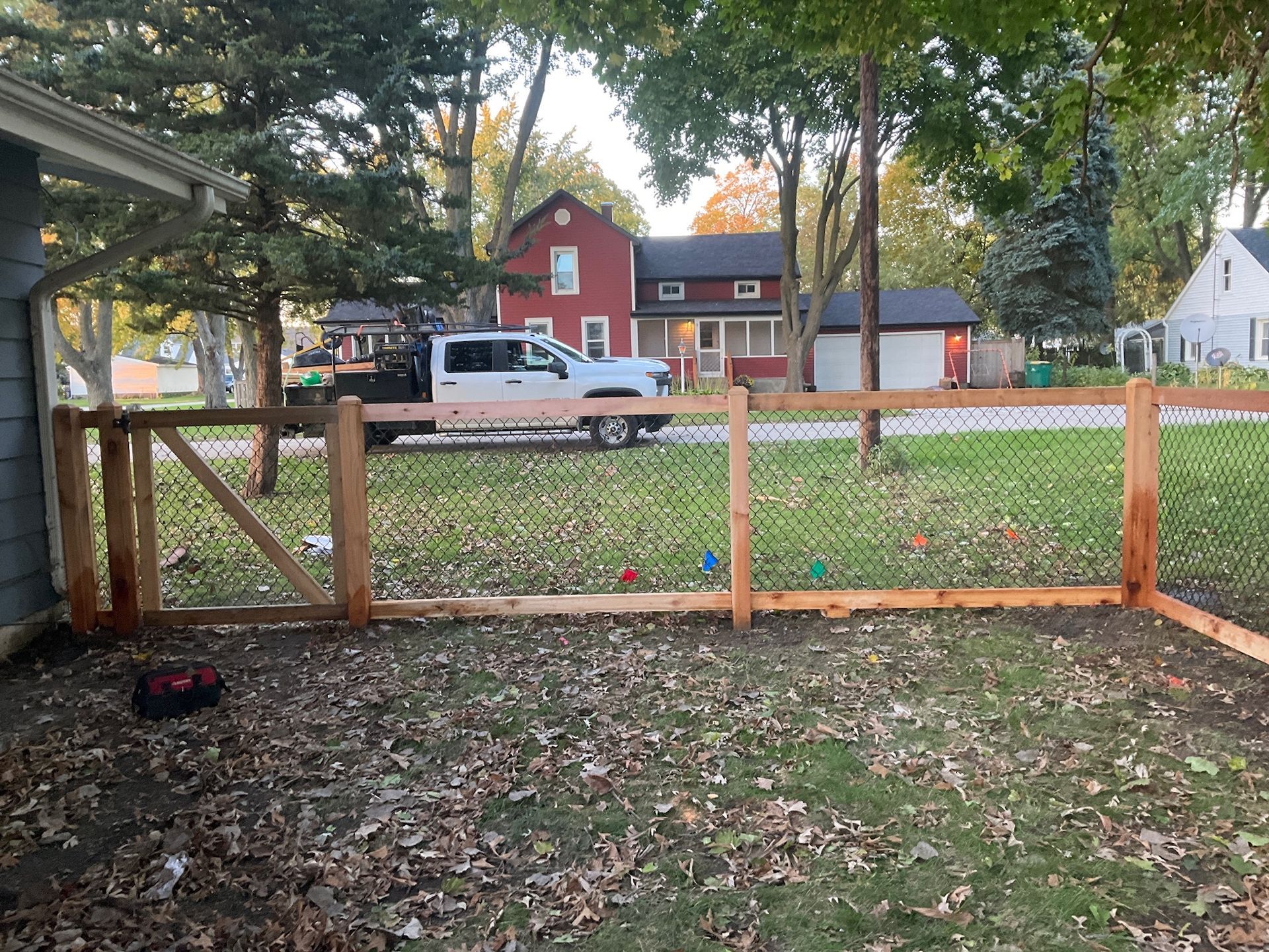 Wooden fence with chain link, white truck parked in front of red house.