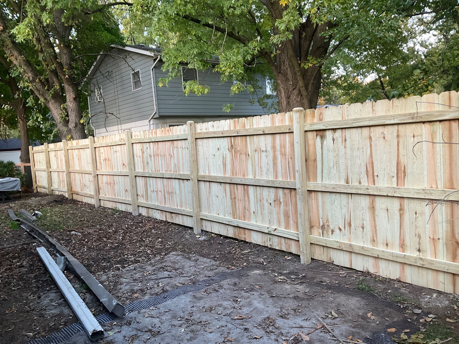 Wooden fence in a yard with a house and trees in the background.