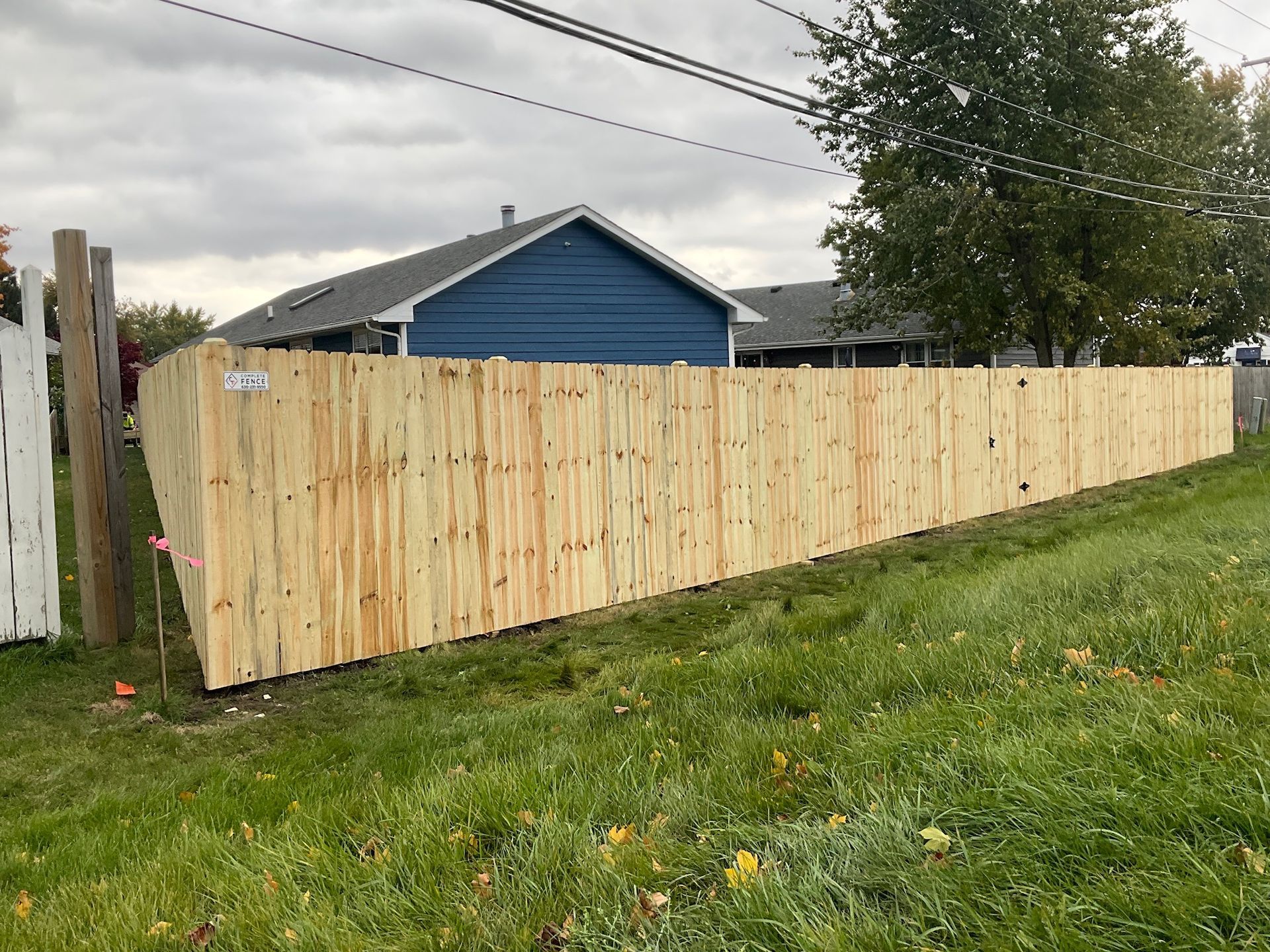 Wooden fence along a green lawn, beside a house with blue siding. Overcast sky.