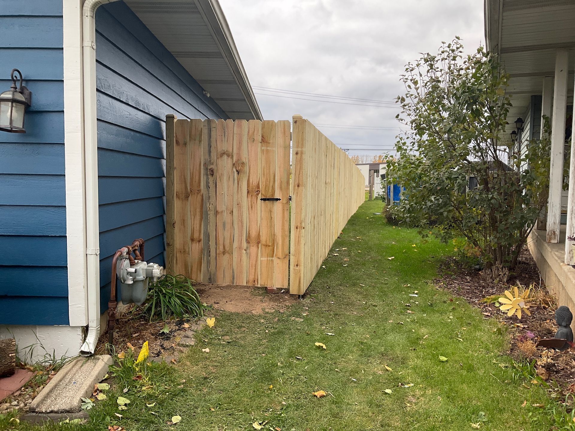 Wooden fence separating two houses with blue siding and green grass.