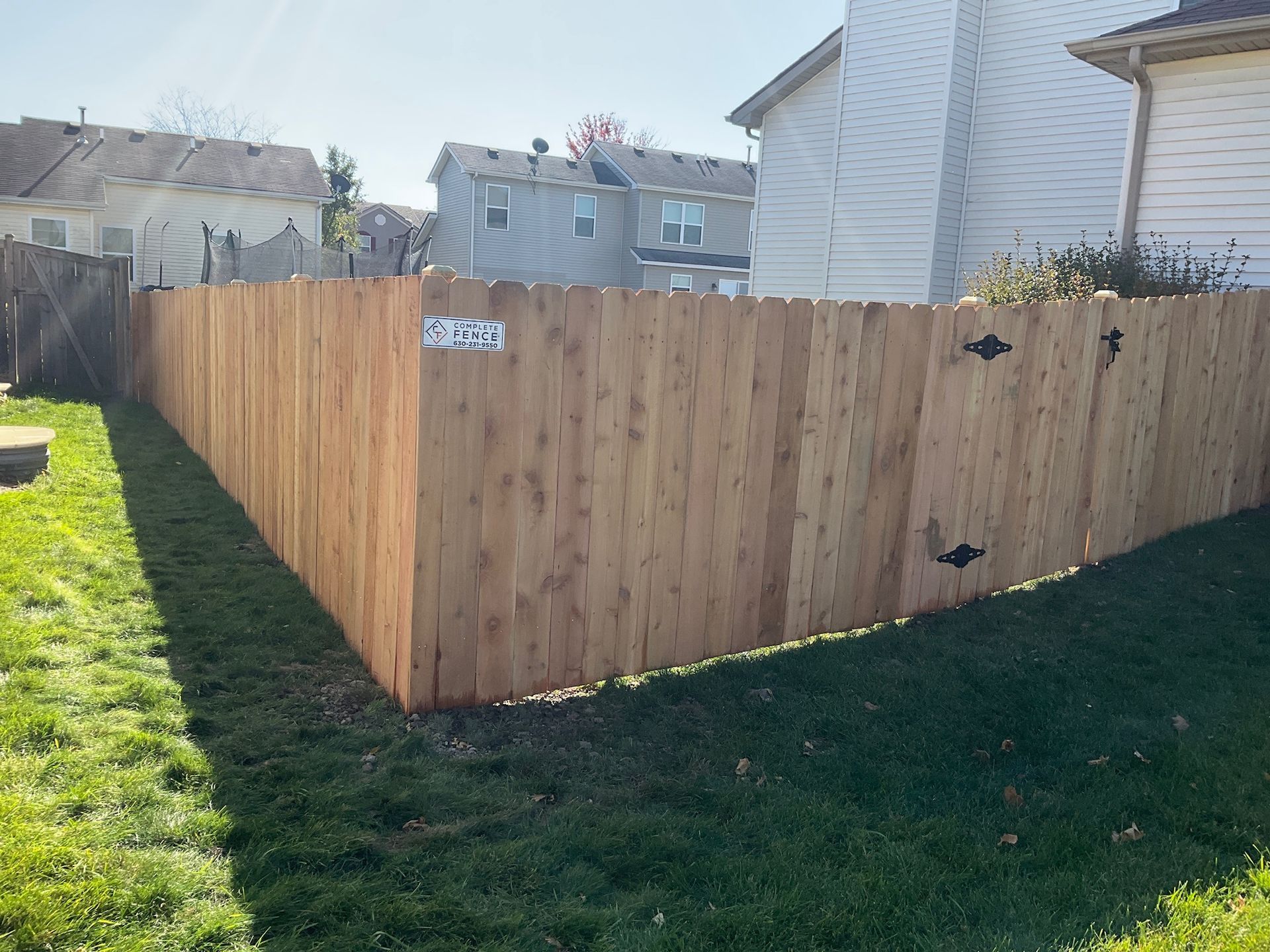 Wooden privacy fence in a grassy yard, with neighboring houses in the background.