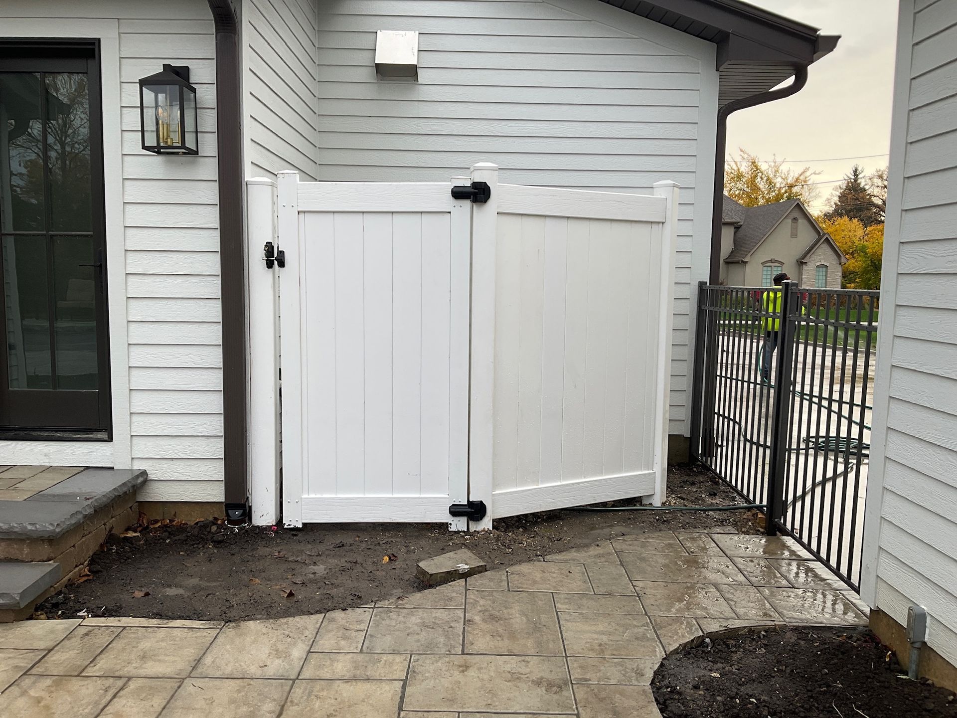 White vinyl gate with black hardware against a white building. Next to a patio and a black fence.