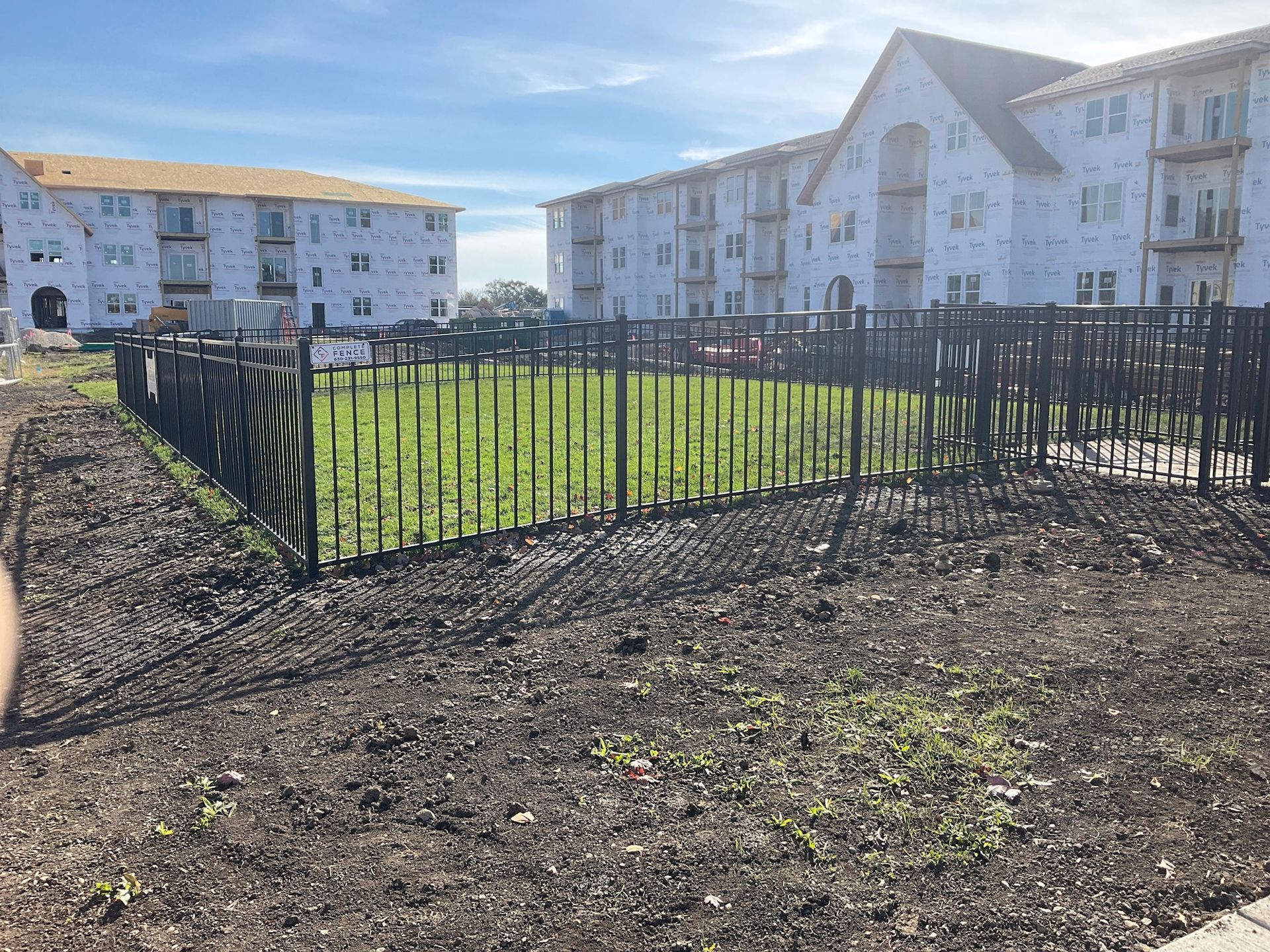A black metal fence encloses a patch of grass. Buildings under construction are in the background.