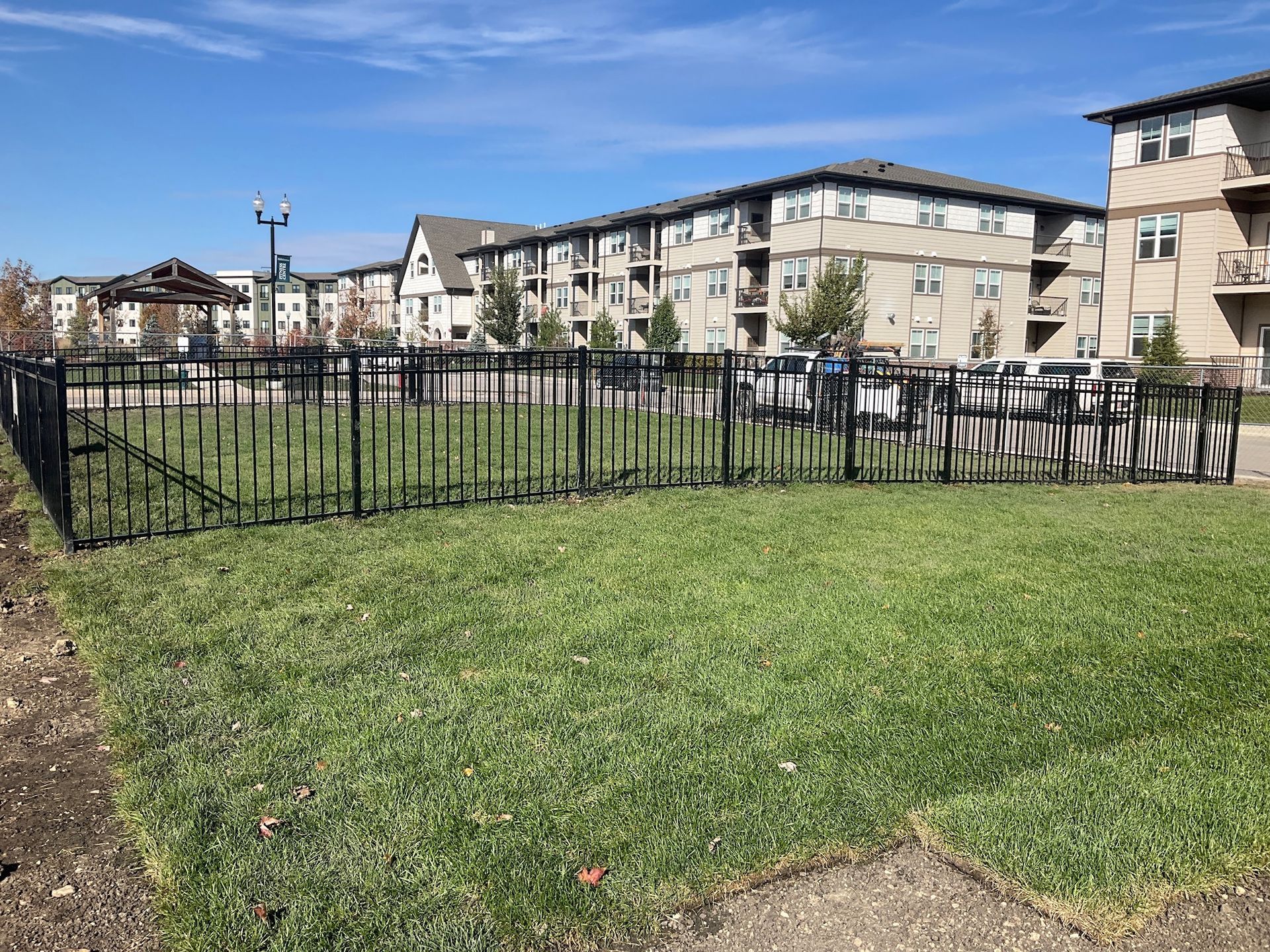 Fenced-in grassy area with apartment buildings in the background on a sunny day.
