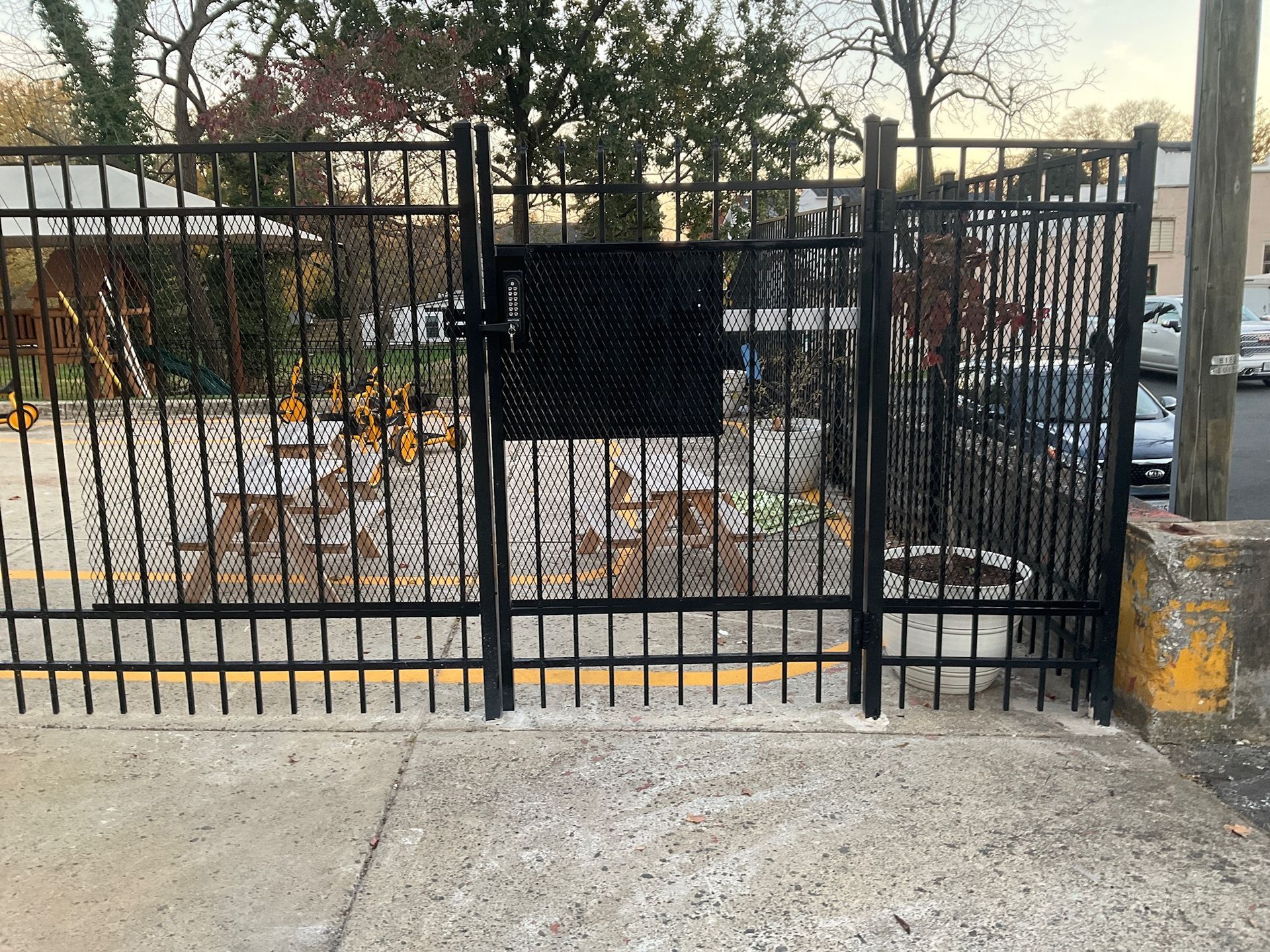 Black metal fence with a gate, concrete walkway, and yellow curb.
