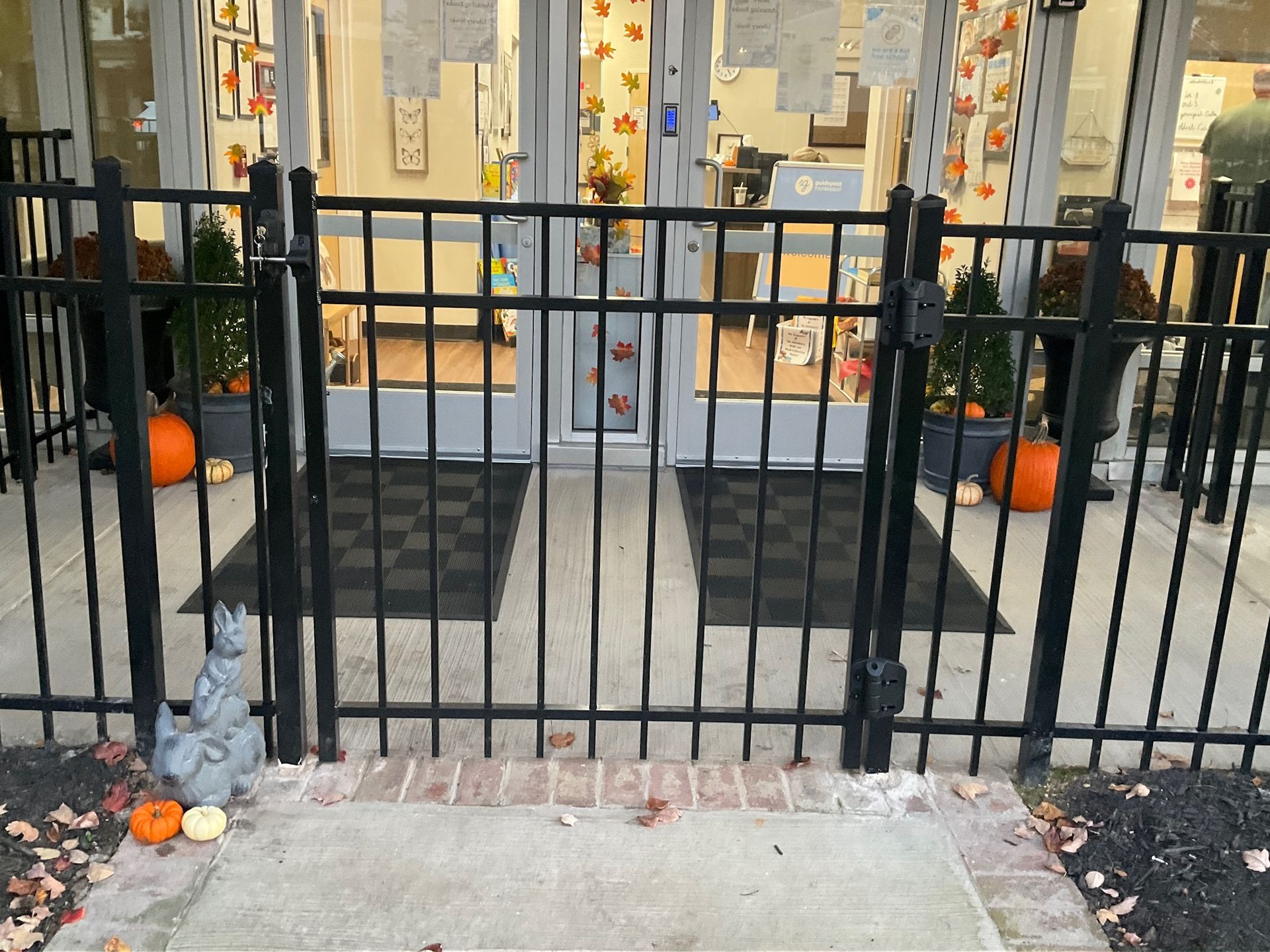 Black metal gate at the entrance to a building decorated with pumpkins and fall leaves.