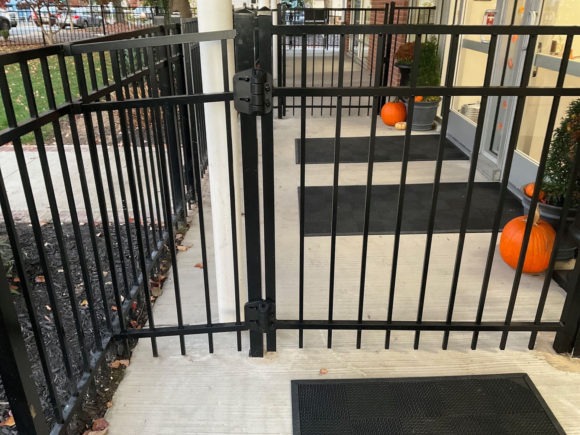 Black metal fence and gate on concrete porch, pumpkins, and a doormat.