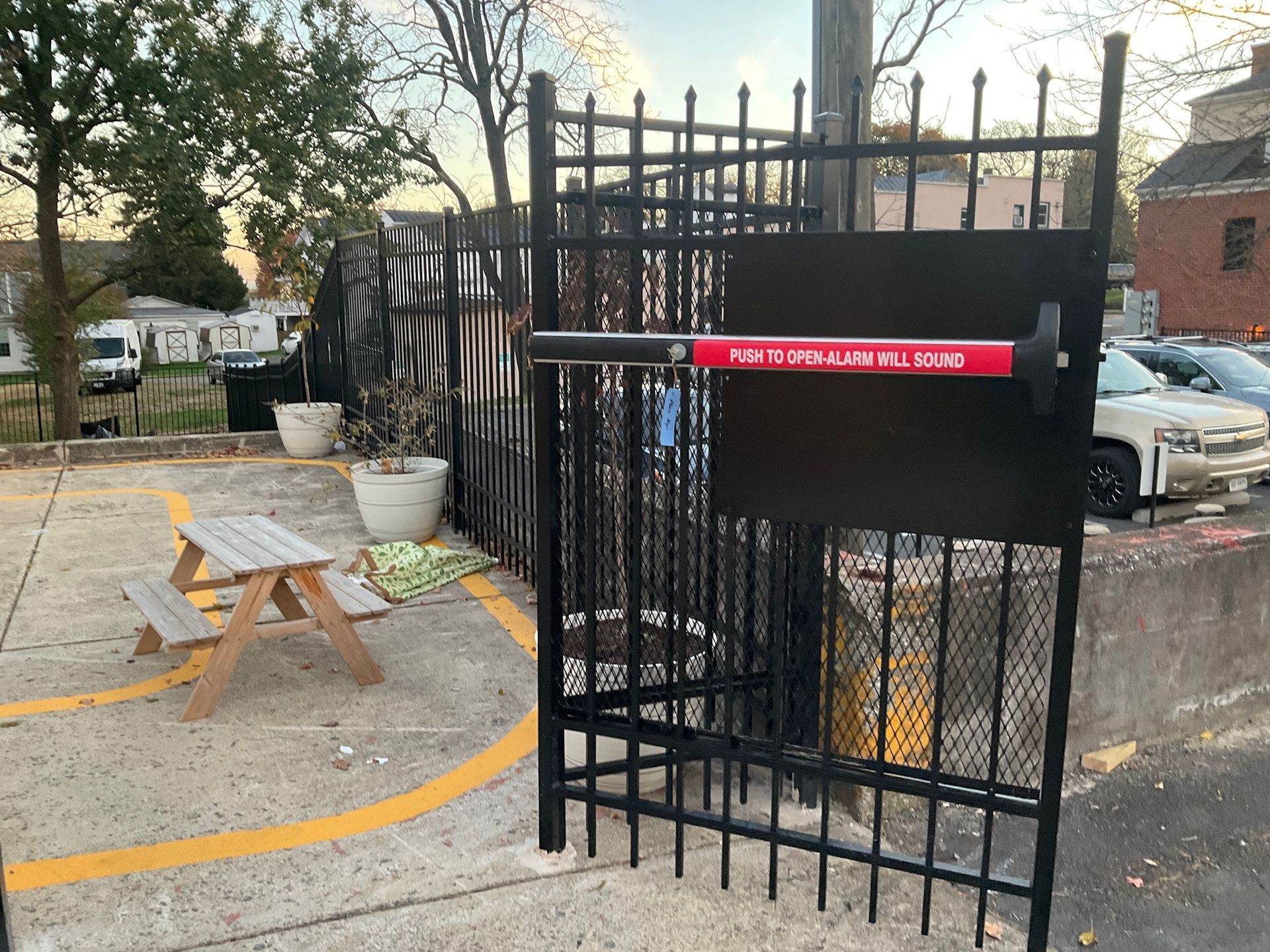 Black metal gate with push bar, picnic table, parking lot.
