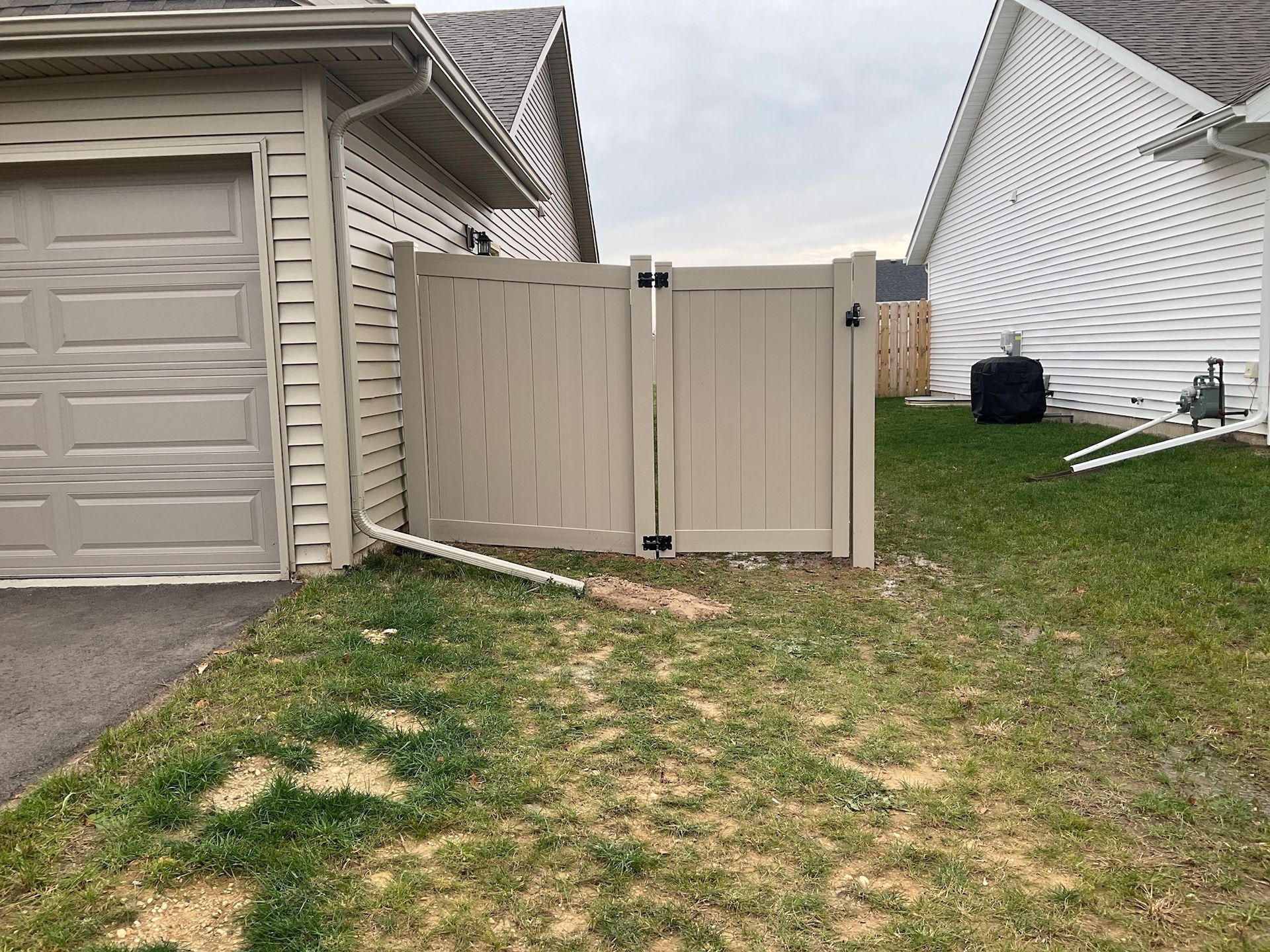 Tan vinyl gate between a garage and house on a grassy lawn.