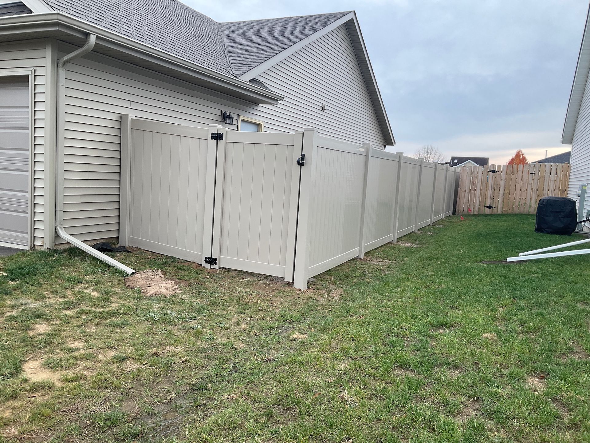 Beige privacy fence in a backyard, beside a house with tan siding and a garage.