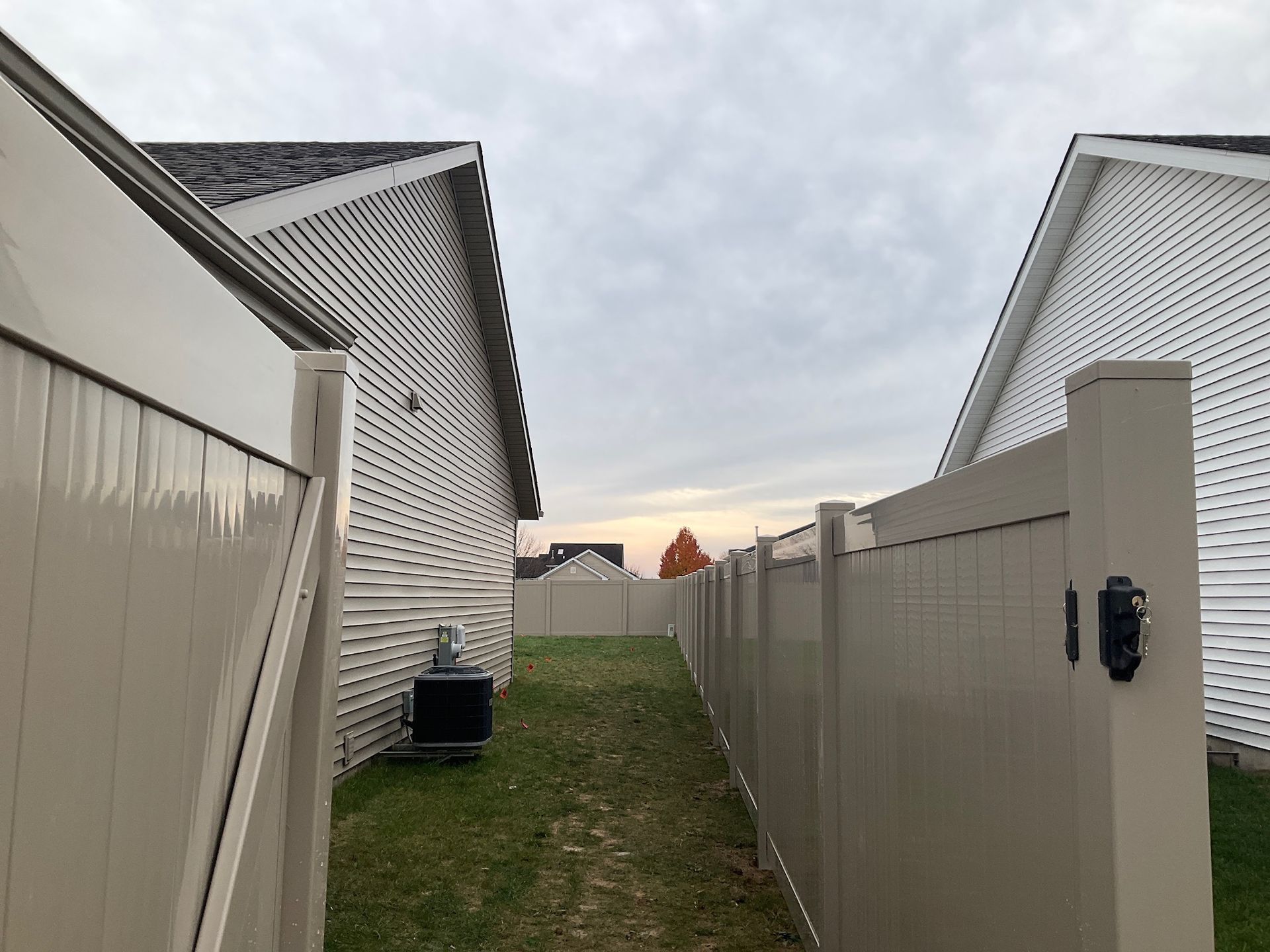 Tan vinyl fence between two white-sided houses under a cloudy sky.