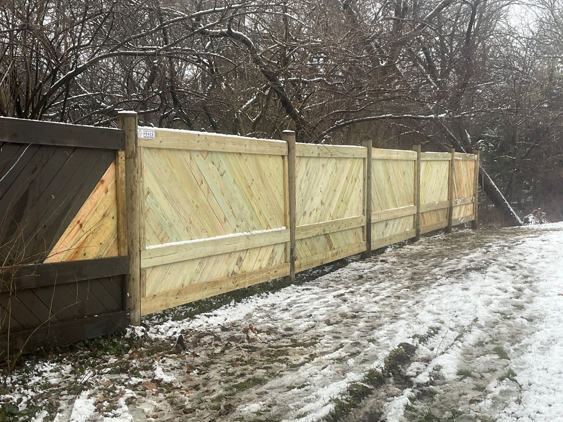 Wooden fence in a snowy, outdoor setting; light colored panels with diagonal design.